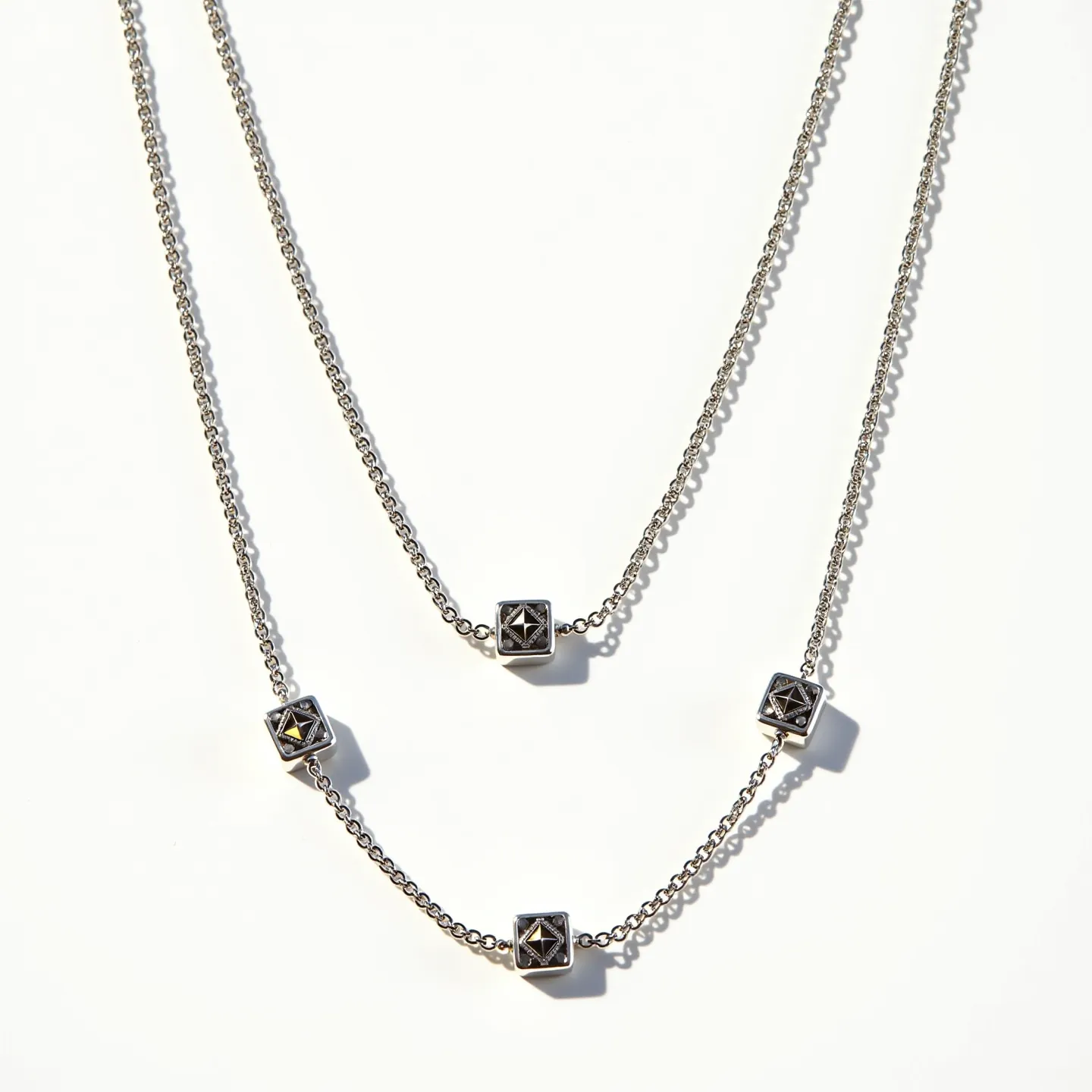 This silver chain features a double-layered design, crafted from a sleek and polished metal, likely sterling silver. Adorning the chain are geometric gemstone settings, likely cubic in shape. Each of these settings houses a single, faceted stone that catches the light, suggesting a prong or bezel setting to secure the gems. The stone's cut appears to be geometric, possibly a square or emerald cut. The chain's fastening and connection to any clasp are generally discreet, emphasizing the elegance and simplicity of the design.