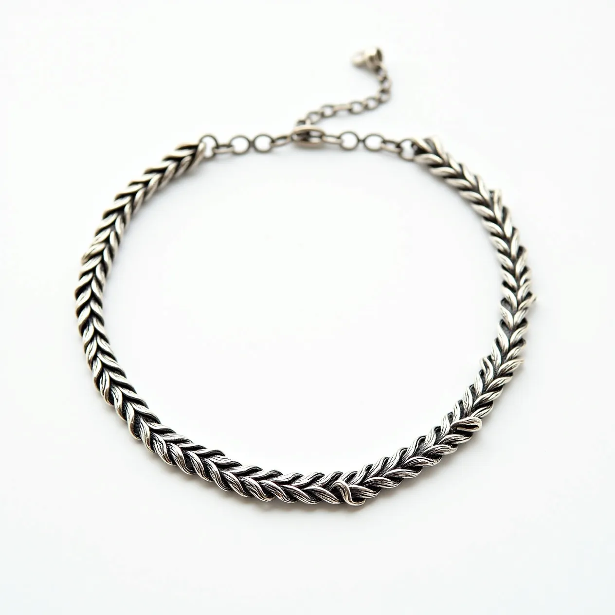 This silver choker necklace features a textured, braided design, crafted from polished silver that showcases intricate detailing along its length. The necklace is made solely from silver, giving it a sleek and elegant appearance. At one end, it includes an adjustable chain segment with several links, allowing for customization of the fit. The clasp is a lobster claw type, providing a secure attachment. The design is sophisticated and versatile, suitable for both casual and formal wear.