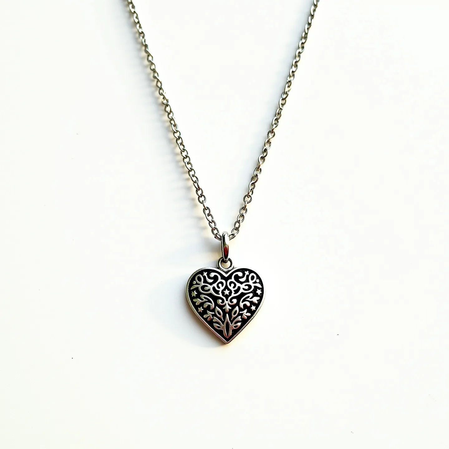 This silver heart necklace features an intricately designed heart-shaped pendant adorned with a delicate filigree pattern. The pendant hangs from a simple silver chain, which is crafted from polished links to provide a subtle shine. The heart design suggests a possible oxidation effect, enhancing the details of the pattern. The necklace is fastened with a classic spring ring clasp, allowing for easy wear and secure closure. The overall elegance of the necklace makes it suitable for both everyday wear and special occasions.