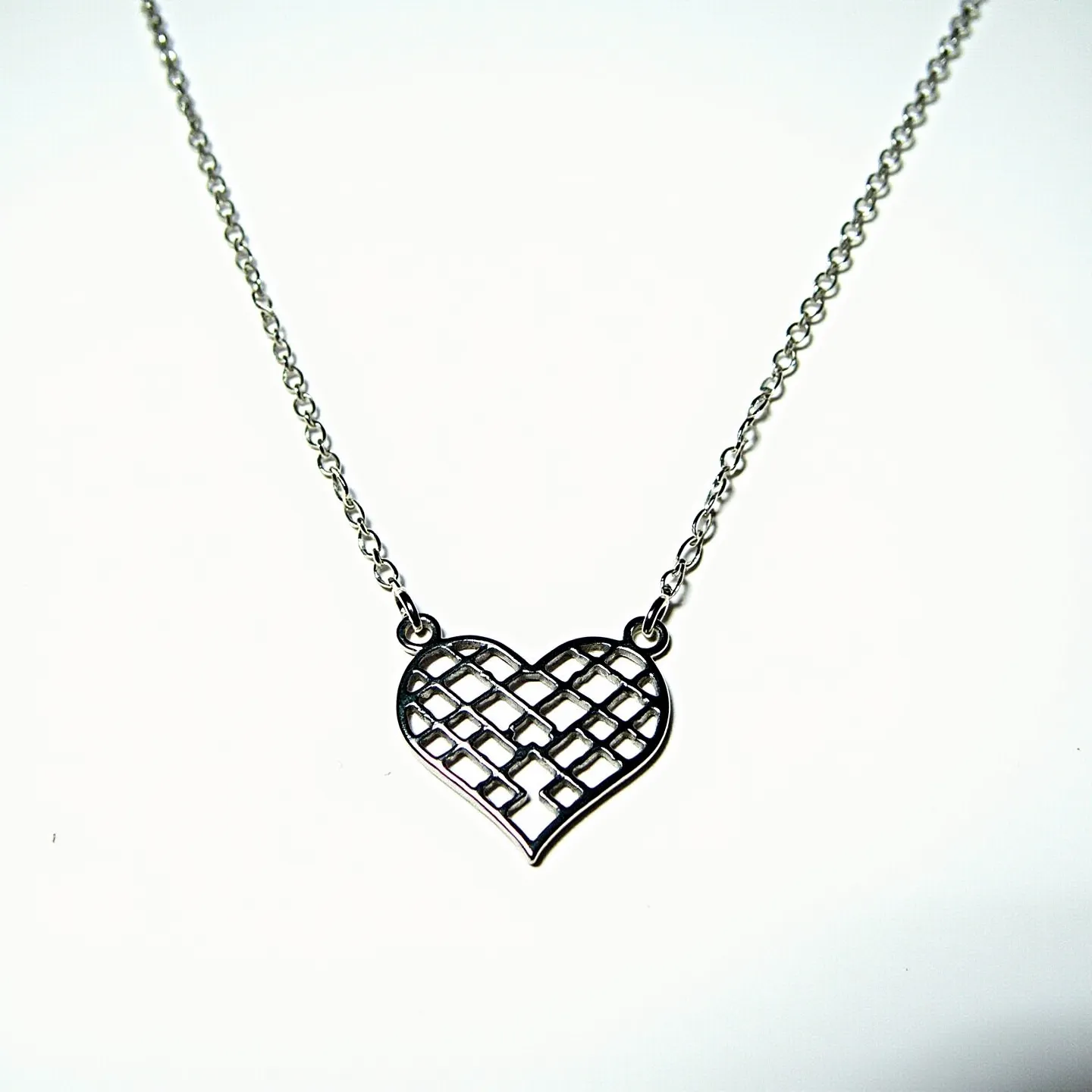 This silver heart necklace features a delicate chain that supports a heart-shaped pendant, crafted from polished silver material. The pendant showcases an open lattice design, giving it a unique and elegant appearance. The heart is attached to the chain with sturdy jump rings on either side, ensuring stability and balance. The fine craftsmanship highlights the intricate lines and smooth edges that define the pendant's aesthetic. The chain is likely secured with a simple, classic clasp to ensure easy wearability and security.