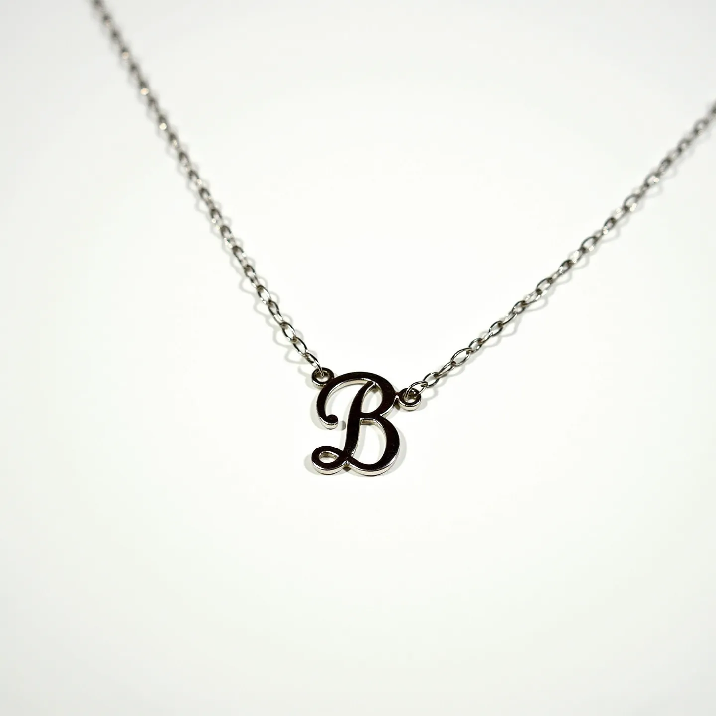 This silver initial necklace features a delicate chain and a prominently displayed capital letter "B" as its centerpiece, crafted in silver. The chain comprises a series of small, interconnected links that provide a refined and elegant appearance. The letter pendant is gracefully integrated into the necklace's design, maintaining a seamless aesthetic. The necklace is fastened with a standard clasp, ensuring ease of wear and security. The minimalist design focuses on the polished shine of the silver, exuding a timeless simplicity.