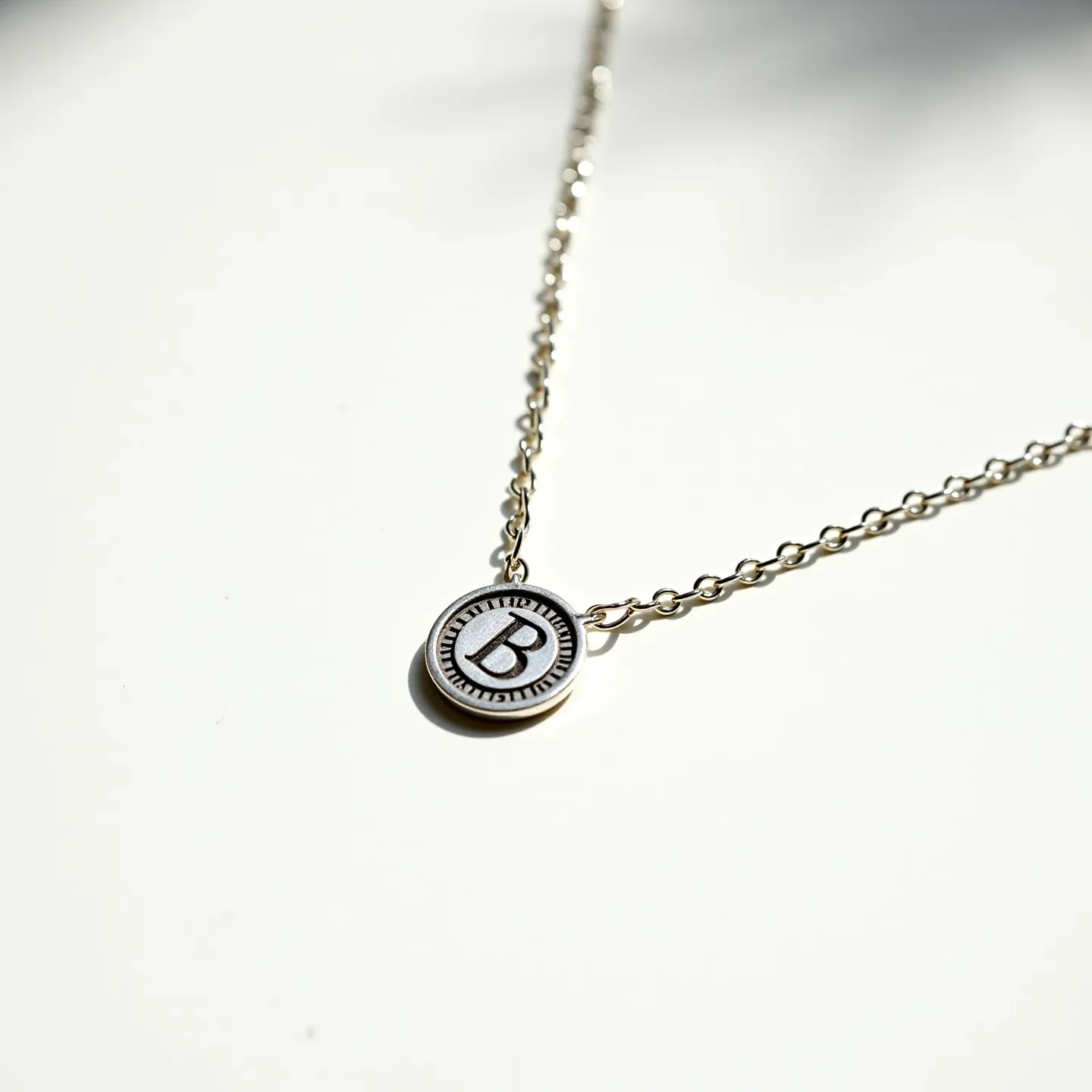 This silver initial necklace features a delicate chain with interlocking links, crafted from a polished silver material. The centerpiece is a round silver pendant, displaying the engraved letter "B" in a bold font. The pendant includes a subtle decorative border, enhancing its visual appeal. The necklace is designed with a simple yet secure clasp, ensuring ease of wear and adjustment. Its minimalist design makes it a versatile accessory for everyday wear or special occasions.