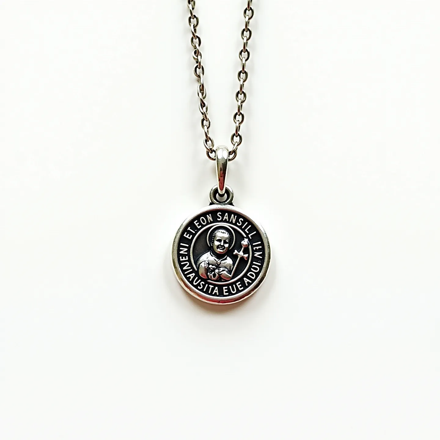 This St. Jude necklace features a round pendant crafted from what appears to be a polished metal, likely silver or stainless steel, showcasing an engraved image of St. Jude in the center. Surrounding the image is an inscription that adds both a decorative and spiritual element. The pendant is attached to a chain with medium-sized, uniform links that complement the pendant's material. The necklace is equipped with a simple bail that connects the pendant to the chain seamlessly. The overall design is elegant and respectful, highlighting the saint's importance while maintaining a minimalist aesthetic.