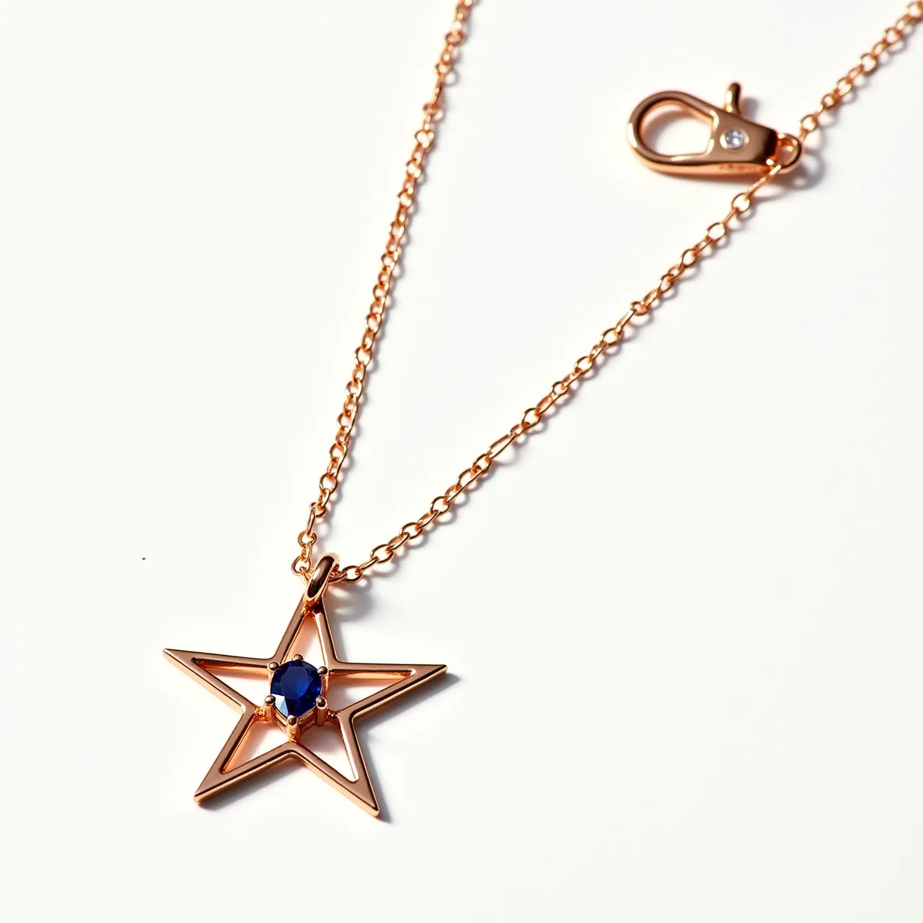 This star necklace features a delicate structure crafted from a polished metal, likely rose gold, highlighting its elegant charm. The centerpiece of the pendant is a blue gemstone, confidently nestled in the star's center with a prong setting that securely holds the stone, which is cut in a round shape, adding a touch of sophistication. The necklace is elegantly suspended from a fine chain that complements the pendant's design. A lobster clasp, adorned subtly with a small, sparkling detail, provides a reliable closure while adding an extra hint of refinement to the overall piece.