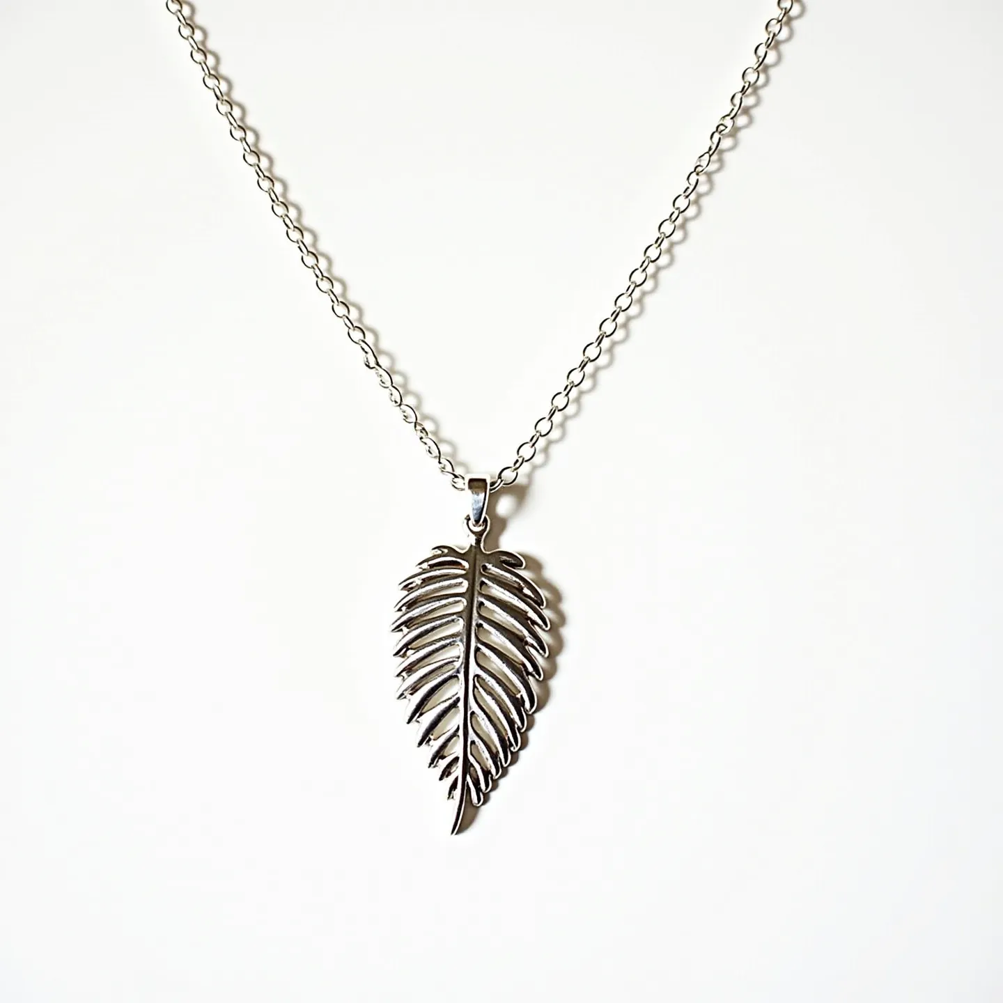 This sterling silver necklace features a delicate, intricately carved leaf-shaped pendant that hangs gracefully from a fine chain. The leaf design showcases elegant grooves, emphasizing its detailed craftsmanship. Suspended from a simple bail, the pendant is eye-catching yet minimalist, allowing the beauty of the sterling silver to shine. The necklace likely includes a standard clasp mechanism, typical for easy wearing and removal, complementing the overall sleek design. No additional gems or stones are present, keeping the focus on the elegant silver leaf motif.