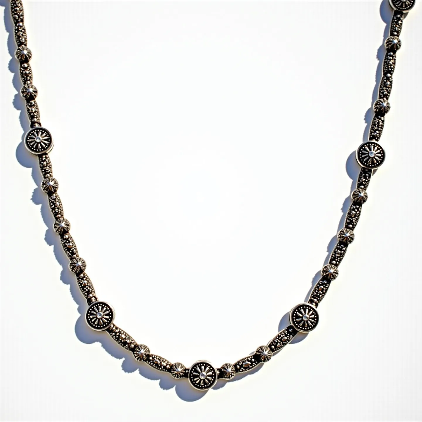 This sterling silver necklace features a series of intricately designed stations composed of small, rounded silver beads interspersed with circular and floral motifs. Some of the circular motifs are adorned with marcasite stones in pavé settings, which enhance the necklace's intricate and elegant design. The symmetry and pattern give it a vintage or classic appeal. The necklace is crafted with meticulous attention to detail, and the metallic shine of the silver is complemented by the subtle sparkle of the marcasite gems. The clasp is not visible, but it likely blends seamlessly with the overall design, ensuring both beauty and security.