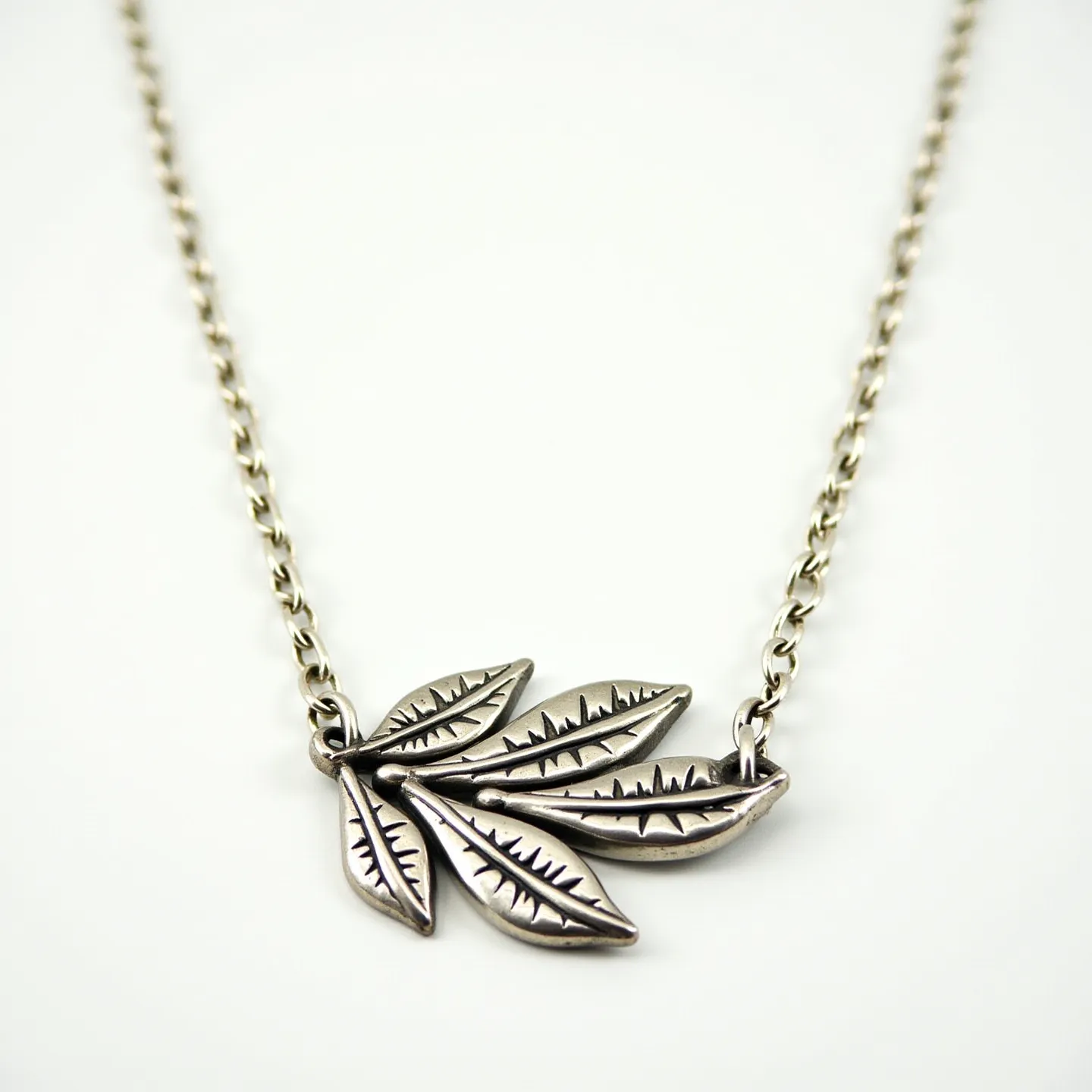 This sterling silver necklace features an intricate design of linked leaves crafted from sterling silver, each leaf detailed with vein-like engravings that give them a lifelike appearance. The necklace has a classic chain link style, with each segment smoothly joined to create a continuous, elegant flow. The main focal point is the leaf motif, positioned centrally to draw attention. It is securely affixed to the chain with a simple loop connection. This necklace is finished with a standard clasp at the back, ensuring it is both easy to fasten and secure during wear.