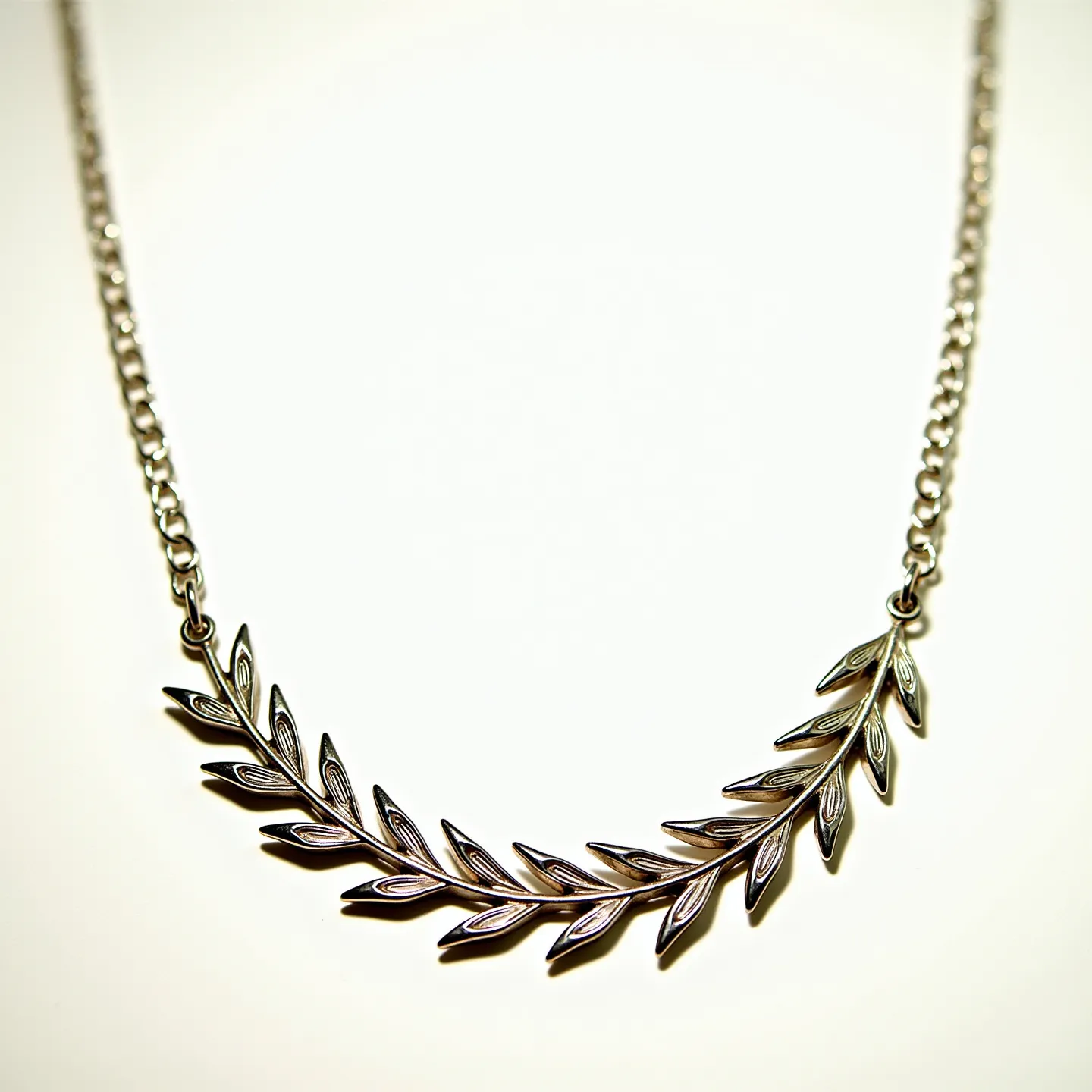 This sterling silver necklace features a delicate design resembling a laurel wreath or leafy branch, with intricately crafted leaf motifs forming the central element. Each leaf is beautifully detailed, adding dimension and elegance to the piece. The necklace is connected by a fine silver chain, which complements the central element's aesthetic seamlessly. A standard clasp completes the design, providing a secure and functional closure. This piece embodies both simplicity and sophistication, making it a versatile accessory for various occasions.