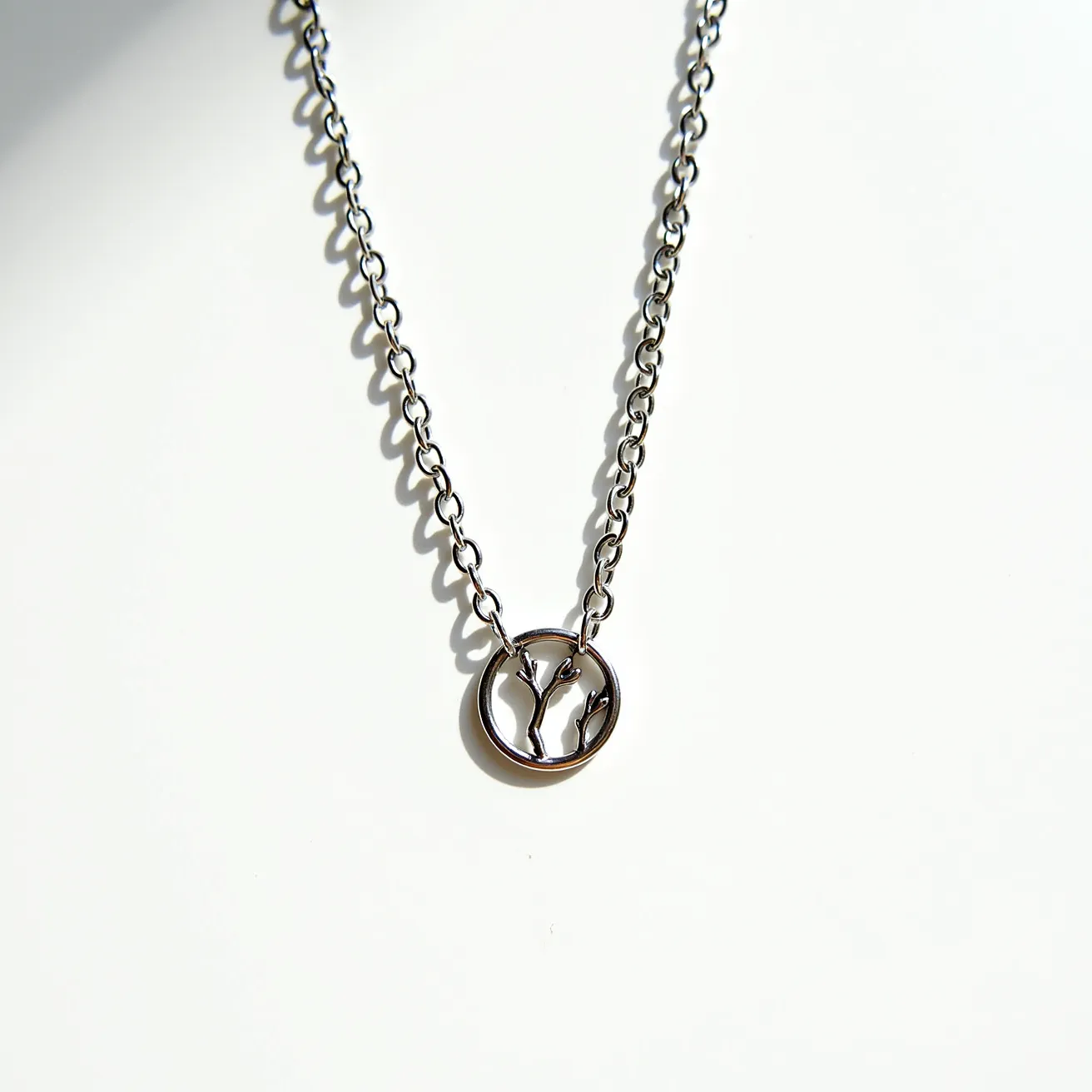 This sterling silver necklace features a delicate chain that supports a circular pendant with an intricate tree branch design at its center. The chain is composed of interlocking links that provide flexibility and durability, reflecting the classic elegance of silver. The pendant, skillfully crafted with a polished finish, is both minimalist and artistic, showcasing the natural beauty of the tree motif. The necklace is secured with a standard silver clasp, ensuring a seamless closure.