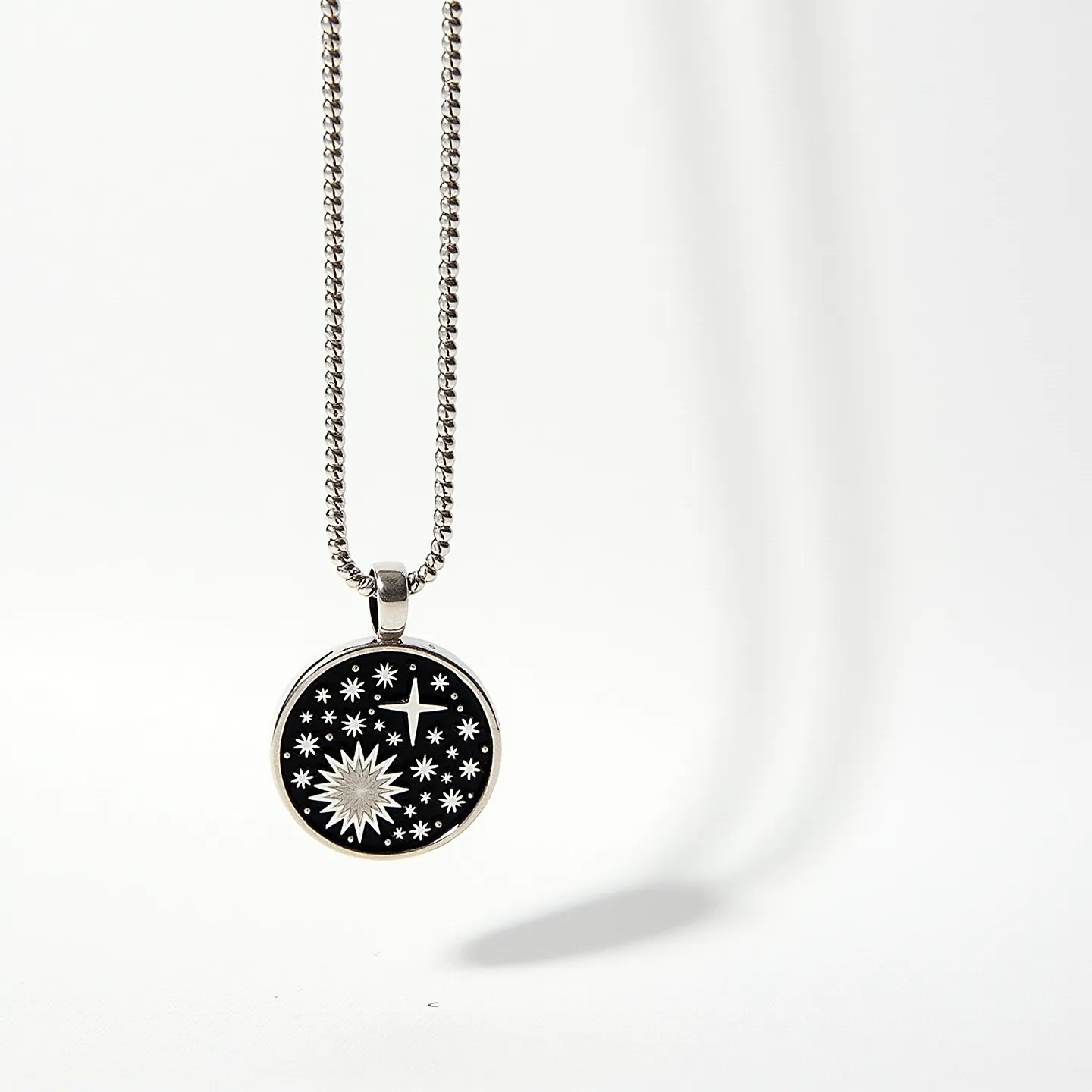 This sterling silver necklace features a classic chain and a round pendant with a black enamel background. The pendant is adorned with intricate celestial designs, including stars and a stylized sun, set in contrasting silver tones for a striking visual effect. The pendant hangs from a bail that securely attaches it to the chain. The necklace's clasp is a standard lobster clasp, ensuring a secure fit when worn. The combination of the silver and black enamel creates a sophisticated and bold statement piece.