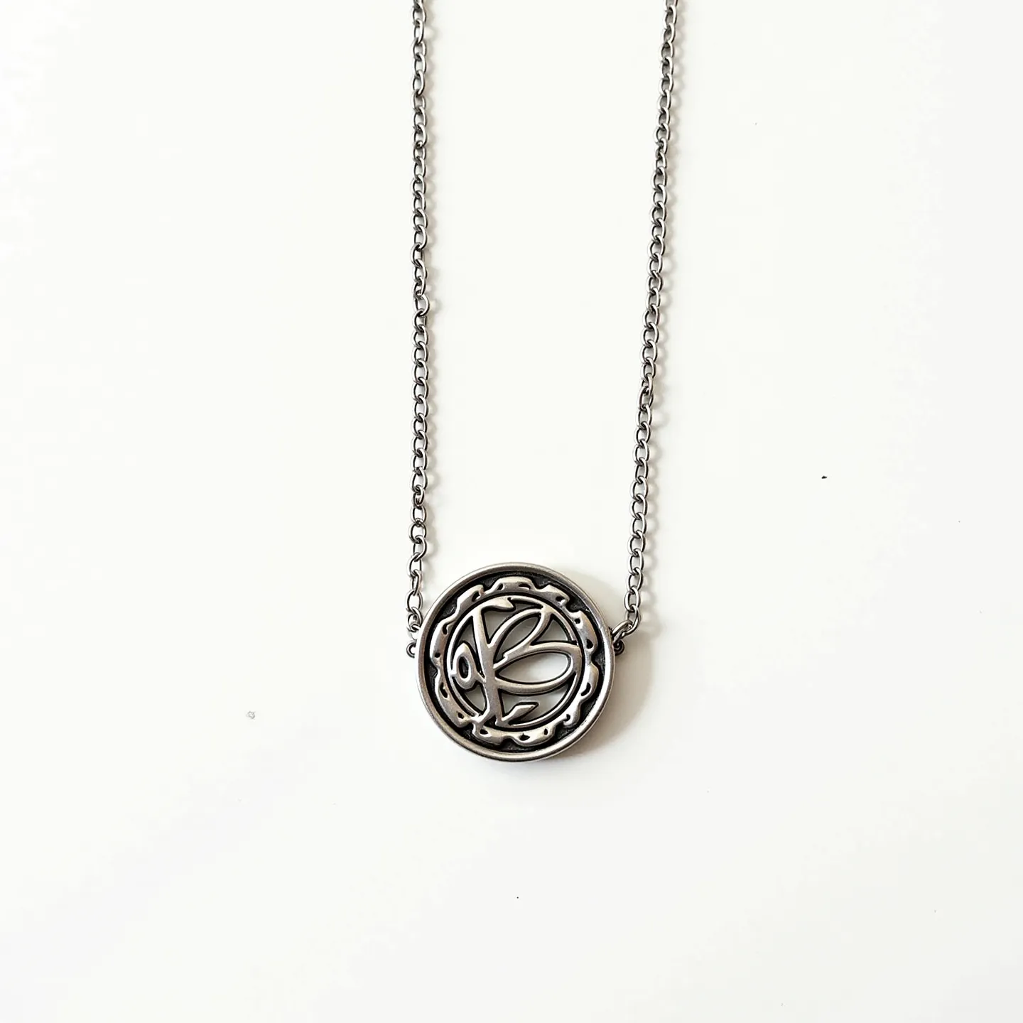 This sterling silver necklace features an intricate pendant with a circular design, showcasing an abstract, artistic motif that is delicately crafted within the confines of the circle. The pendant does not include any gemstones, leaving the attention solely on the craftsmanship of the silverwork. The chain is a simple link chain, seamlessly attached to the pendant on either side, allowing it to hang evenly. The necklace likely uses a standard clasp for fastening, consistent with similar pieces in sterling silver jewelry.