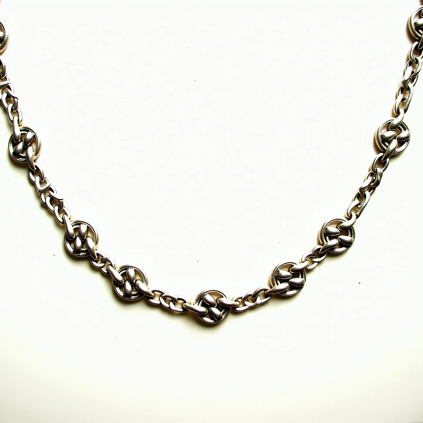 This sterling silver necklace features intricately designed links that are interconnected with larger, decorative circular elements resembling Celtic knots or woven designs. The links are crafted from polished sterling silver, providing a sleek and reflective appearance. Each of the decorative circles is evenly spaced along the chain, adding a rhythmic pattern to the overall design. The necklace is finished with a clasp that seamlessly integrates with the rest of the piece, ensuring both security and visual coherence.