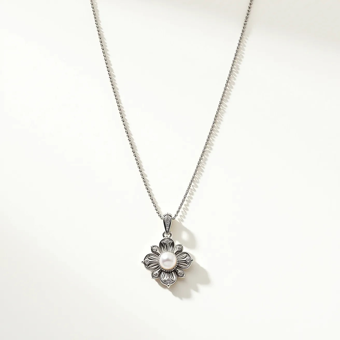 This sterling silver necklace features a delicate chain that is elegantly paired with a floral pendant design. At the center of the flower-shaped pendant is a round, lustrous pearl, which serves as the focal point. The petals of the flower are intricately carved, showcasing detailed craftsmanship that highlights the natural beauty of the pearl. The pendant is attached to the chain with a decorative bail that complements the overall design. The necklace is completed with a secure clasp, ensuring it stays elegantly in place when worn.