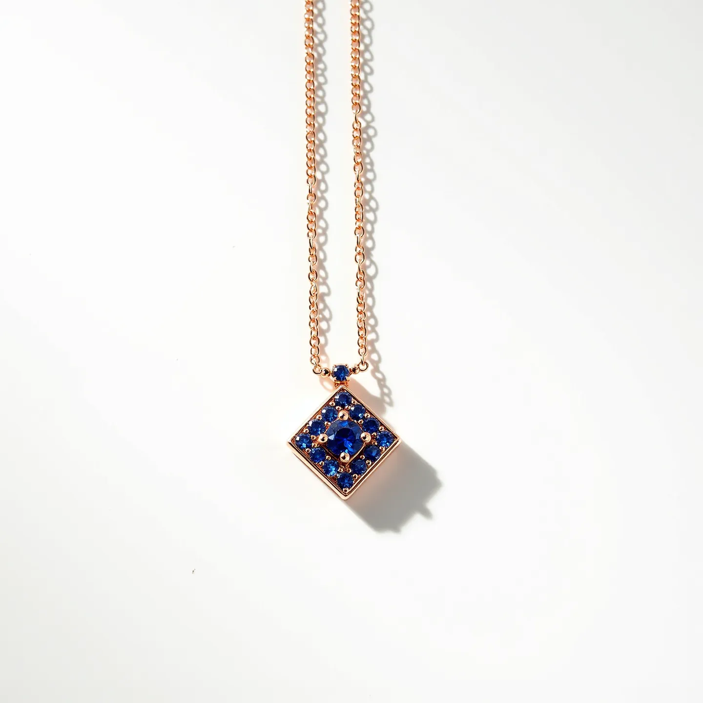 This stone necklace features a delicate chain, likely made of a gold or gold-toned metal, supporting a diamond-shaped pendant adorned with multiple deep blue stones, possibly sapphires or similar gemstones. The stones are round-cut and set closely together in a symmetrical pattern, with a focal stone in the center surrounded by smaller ones, all secured with prongs in a bezel setting. The chain connects seamlessly to the pendant through a small jump ring, enhancing the elegant and refined look of the piece.