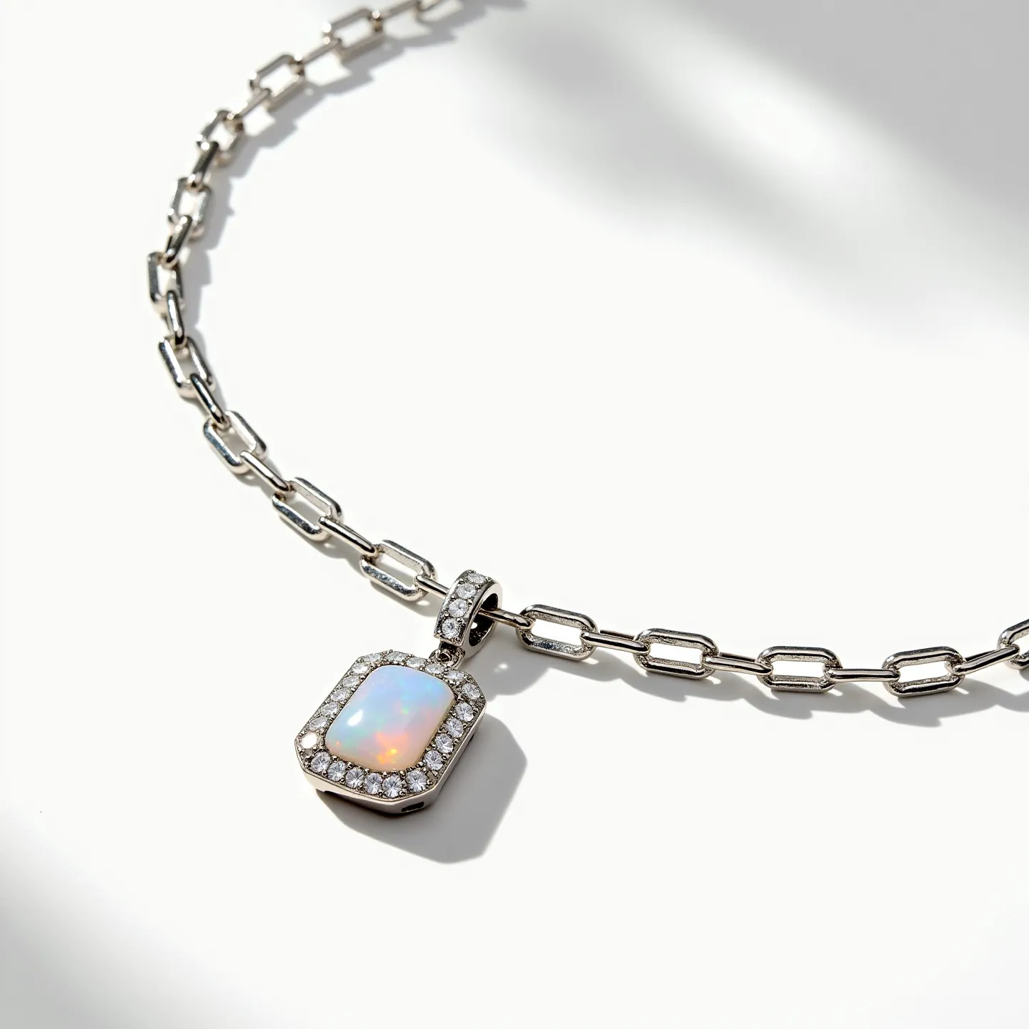 This stone necklace features a striking rectangular opal pendant, showcasing a soft play of colors that reflects light hues. The opal is surrounded by a halo of small, round-cut diamonds set in a neat pave setting, adding a touch of elegance and sparkle. The pendant is attached to a solid silver-tone chain composed of elongated, rectangular links, which offers a modern and refined look. The necklace likely features a clasp that is both secure and easy to operate, ensuring both functionality and style.