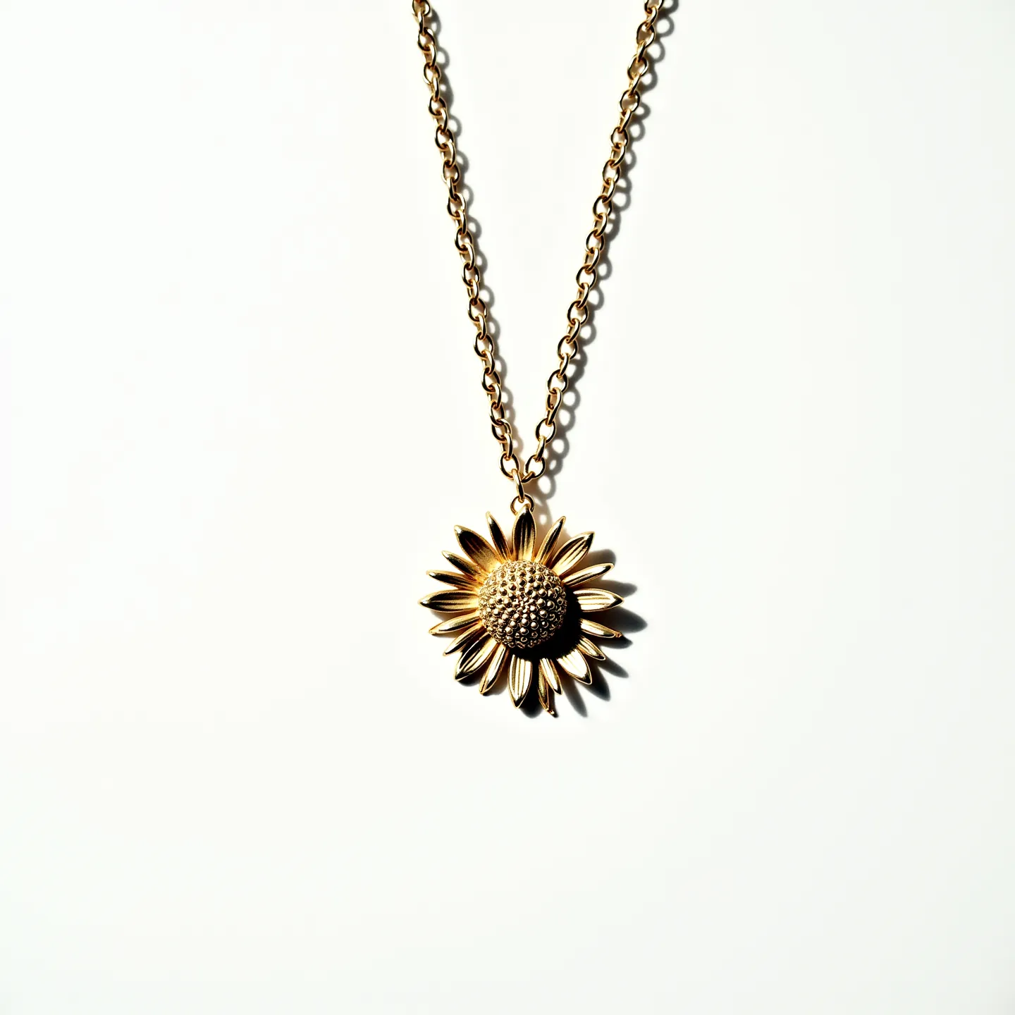 This sunflower necklace features an intricately designed pendant crafted in a golden metal, forming the shape of a sunflower with textured petals radiating from a detailed center. The pendant hangs from a gold-toned chain, which consists of interlocking links that provide a classic and versatile look. It is equipped with a simple lobster clasp for securing the necklace around the neck. There are no visible gemstones or additional embellishments, which highlights the elegant simplicity of the sunflower design.