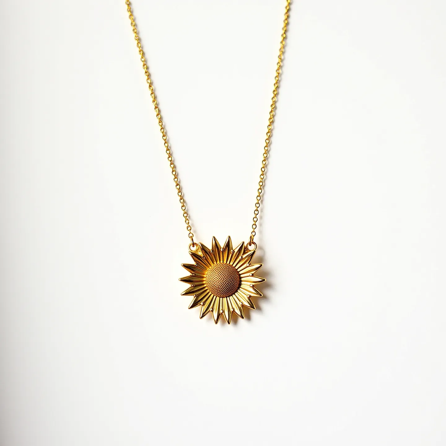 This sunflower necklace features a striking pendant crafted in a golden material, which emulates the natural beauty of a sunflower with detailed and textured petals radiating from a central, textured disc. The pendant is suspended from a delicate and matching gold-colored chain, seamlessly attached at either end of the flower. It appears to be constructed without any visible gems, emphasizing the simplicity and elegance of the sunflower's form. The necklace is likely to have a simple clasp at the back, typical of many fine jewelry pieces, allowing for ease of wear.