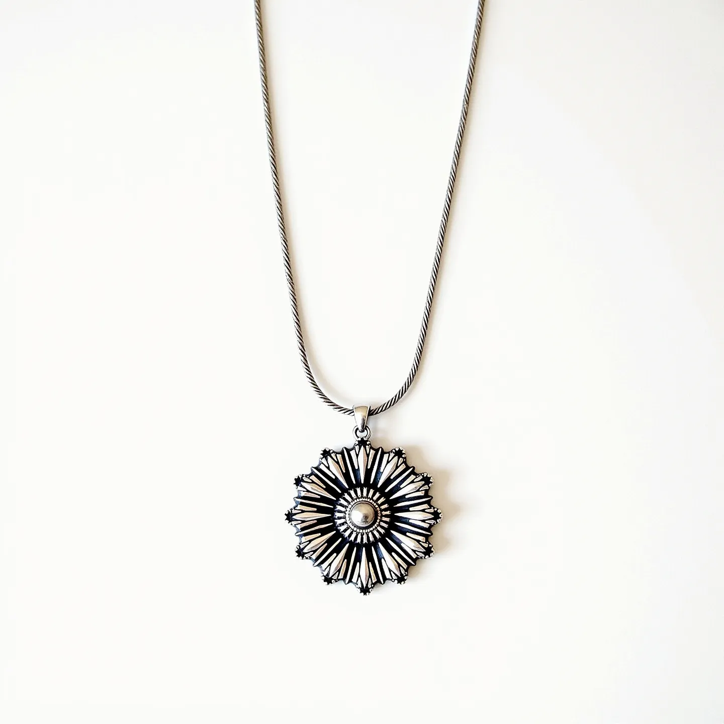 This sunflower necklace features an intricate pendant design that resembles the vibrant petals of a sunflower, radiating from a textured circular center. Made from what appears to be a silver-toned metal, the pendant showcases detailed craftsmanship with its layered, cut-out pattern. The pendant is attached to a twisted, rope-style chain that complements the ornate design, giving it a harmonious look. The necklace is likely fastened with a standard lobster clasp, providing a secure and classic closure. The overall aesthetic of the necklace is both elegant and bold, making it a distinctive accessory.