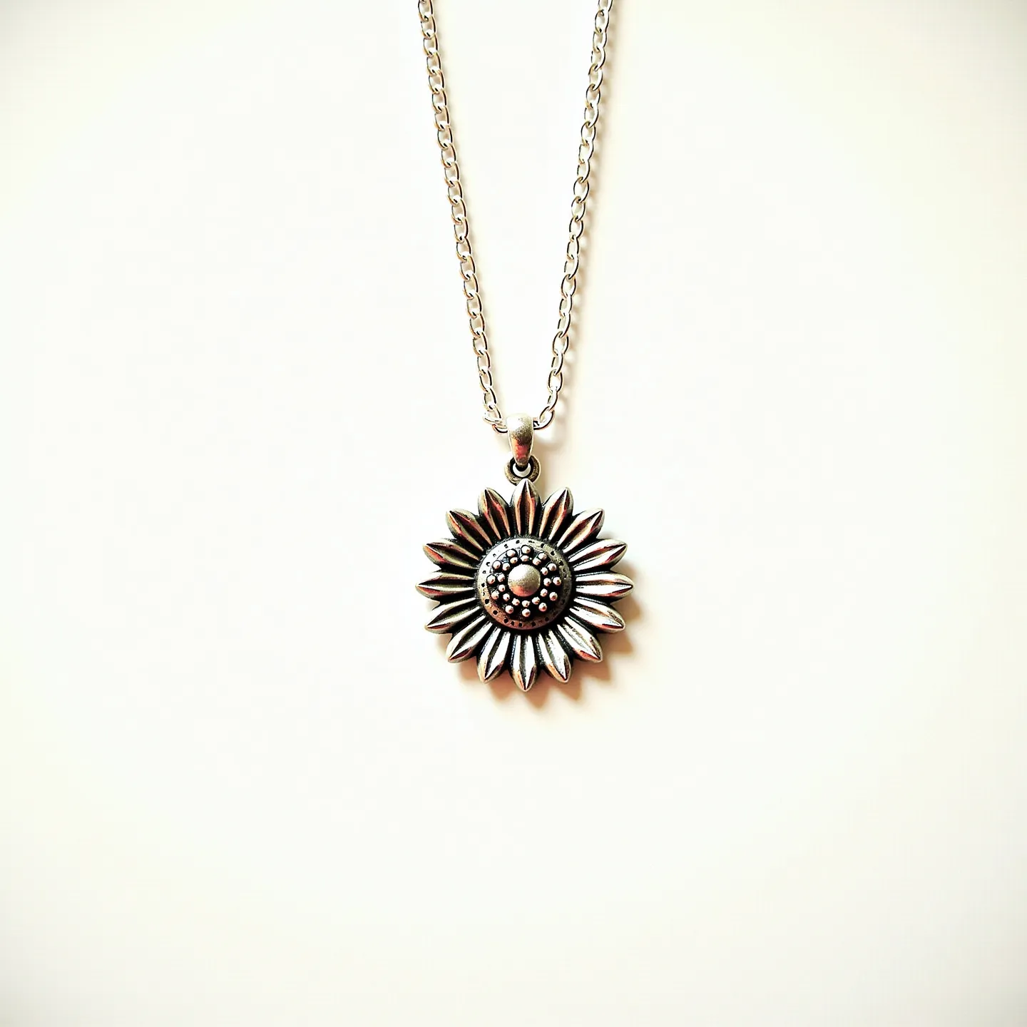 This sunflower necklace features a detailed pendant crafted in a metallic material, possibly silver or a silver-toned alloy, that highlights its intricate petal design and a textured center resembling a sunflower’s core. The pendant hangs from a simple chain with a uniform link pattern, suggesting durability and elegance. The necklace is secured with a standard clasp mechanism, ensuring ease of wear. The design captures the beauty of nature with a classic, timeless appeal, making it a versatile accessory for various styles.