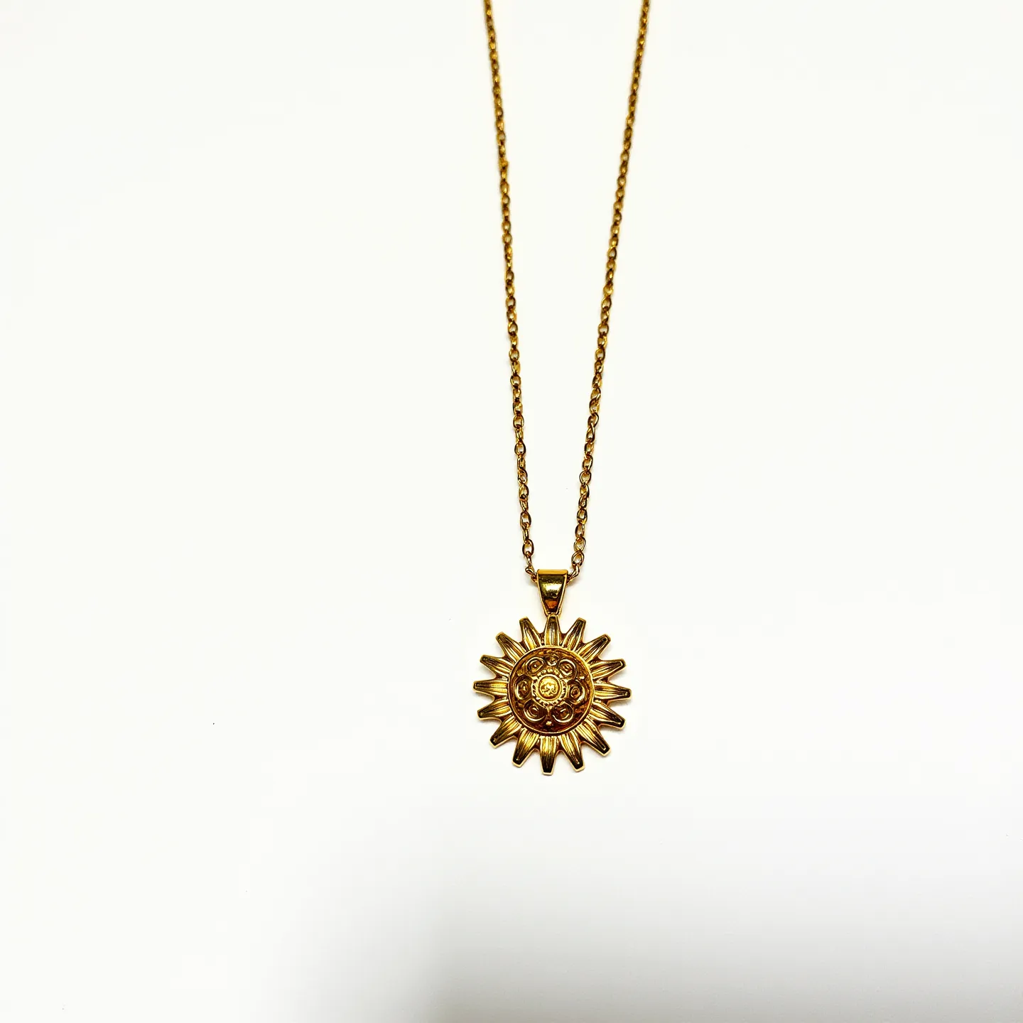 This sunflower necklace features a pendant intricately designed in the shape of a sunflower, crafted from a gold-toned metal that gives it a bright and elegant appearance. The pendant is suspended from a matching gold-toned chain, which is delicate yet sturdy, highlighting the detailed artistry of the sunflower petals. The center of the flower includes small, decorative elements that add texture and dimension, though no specific gemstones are present. The necklace is equipped with a small bail, seamlessly connecting the pendant to the chain, and it likely secures with a traditional clasp, ensuring ease of wear and reliability. Overall, this necklace exudes a charming and timeless aesthetic.