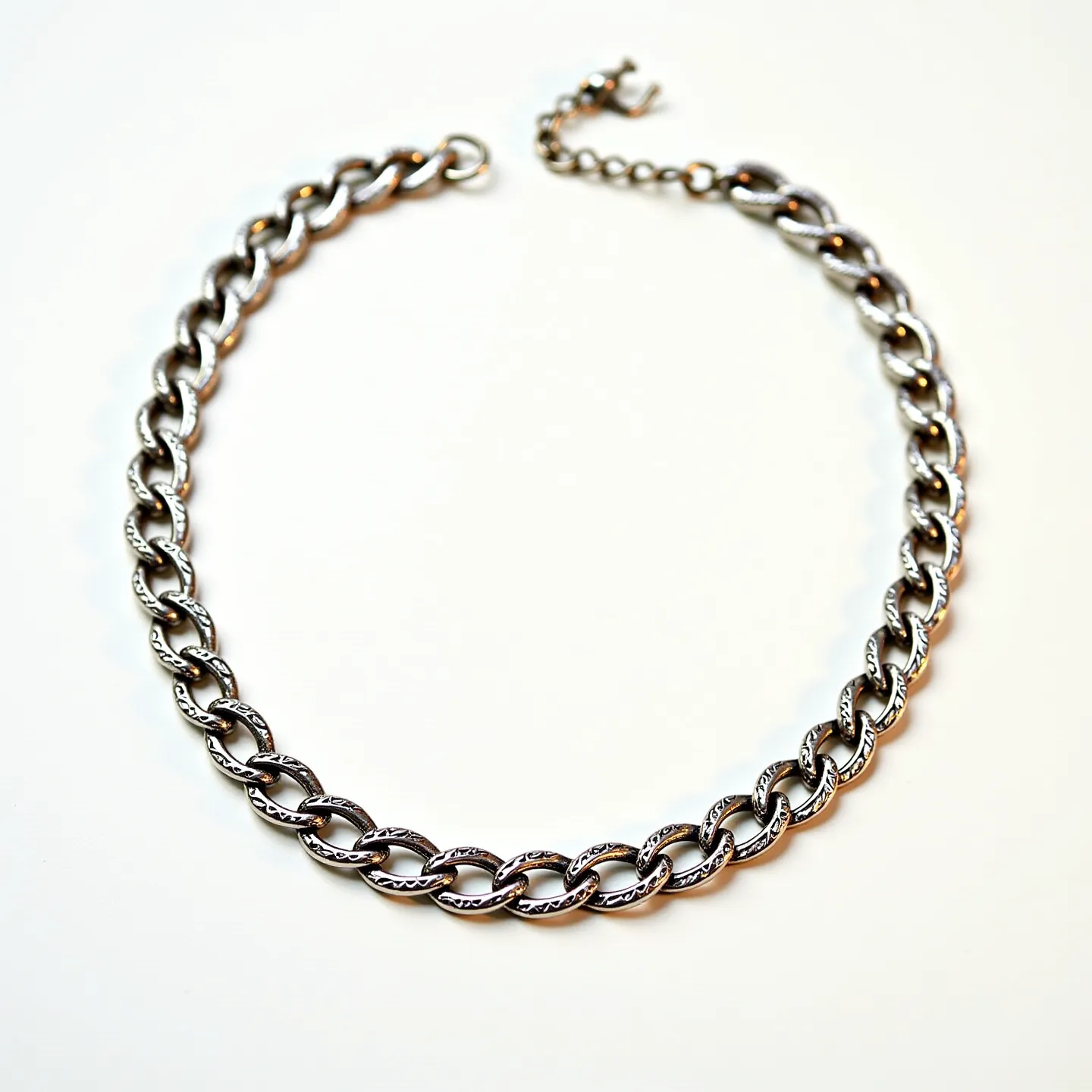 This thick chain necklace features chunky interlocking links made of a silver-toned metal, giving it a bold and polished appearance. The links are substantial, providing a sturdy and fashionable look, and showcase a uniform design throughout the piece. The necklace is finished with a lobster clasp, allowing for secure fastening and ease of wear. A short extender chain at the end provides some adjustability in length, adding to the versatility of the necklace.