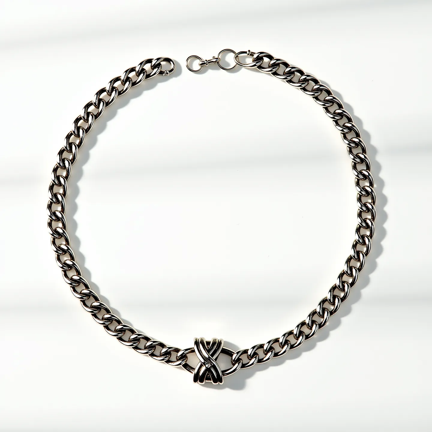 This thick chain necklace features interlocking rounded links with a polished silver-toned finish, adding a sleek and modern appeal. At its center is a larger, distinctive central accent piece with intertwined designs that suggest a figure-eight or infinity motif, providing a focal point without the use of gems or stones. The necklace is equipped with a circular clasp, likely a lobster claw or spring ring, ensuring a secure and easy closure. This design combination makes the necklace a bold yet versatile accessory suitable for various styles and occasions.