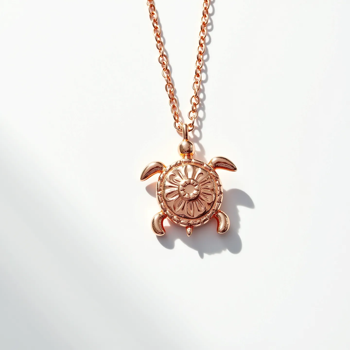 This turtle necklace features a charming turtle pendant crafted from a metal that appears to have a rose gold hue, adding warmth to its appearance. The pendant is designed with a symmetrical floral pattern etched on the turtle's shell, contributing to its intricate and elegant aesthetic. The chain is consistent in style, with oval links that complement the pendant's design. The pendant is attached to the chain through a simple loop that allows for smooth movement and a seamless look. There are no noticeable gemstones or intricate settings on the pendant itself. The necklace is secured with a standard clasp, offering practicality and ease of wear.