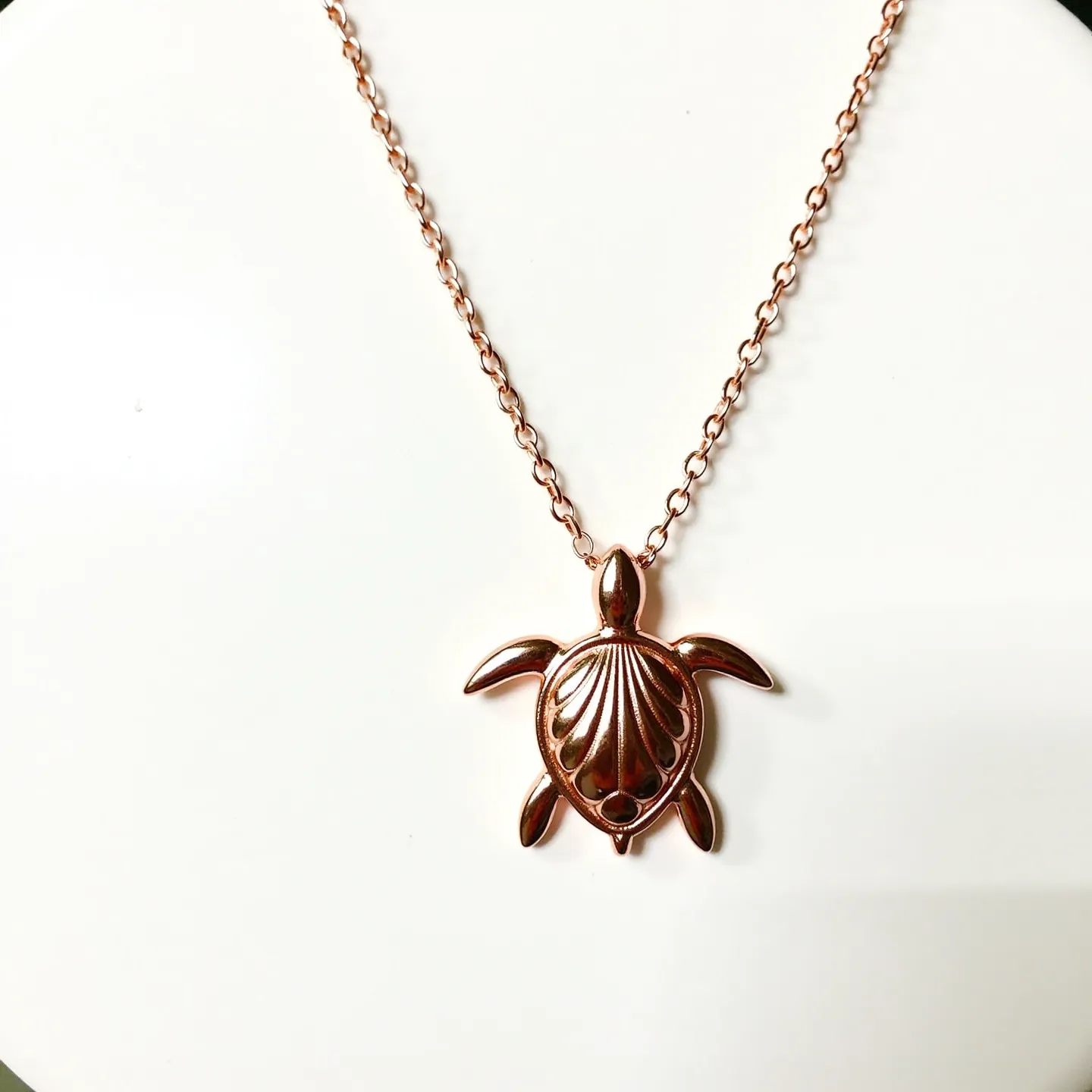 This turtle necklace features a beautifully crafted pendant in the shape of a turtle, with a polished rose gold finish that highlights its elegant design. The pendant is suspended from a delicate chain that also shares the same rose gold hue, adding to its cohesive and sophisticated appearance. The front of the turtle shell is adorned with a subtle, engraved pattern, enhancing its visual appeal. This necklace employs a simple, yet secure lobster clasp, ensuring easy wearability. The overall design exudes a sense of charm and refinement, making it a versatile accessory for various occasions.