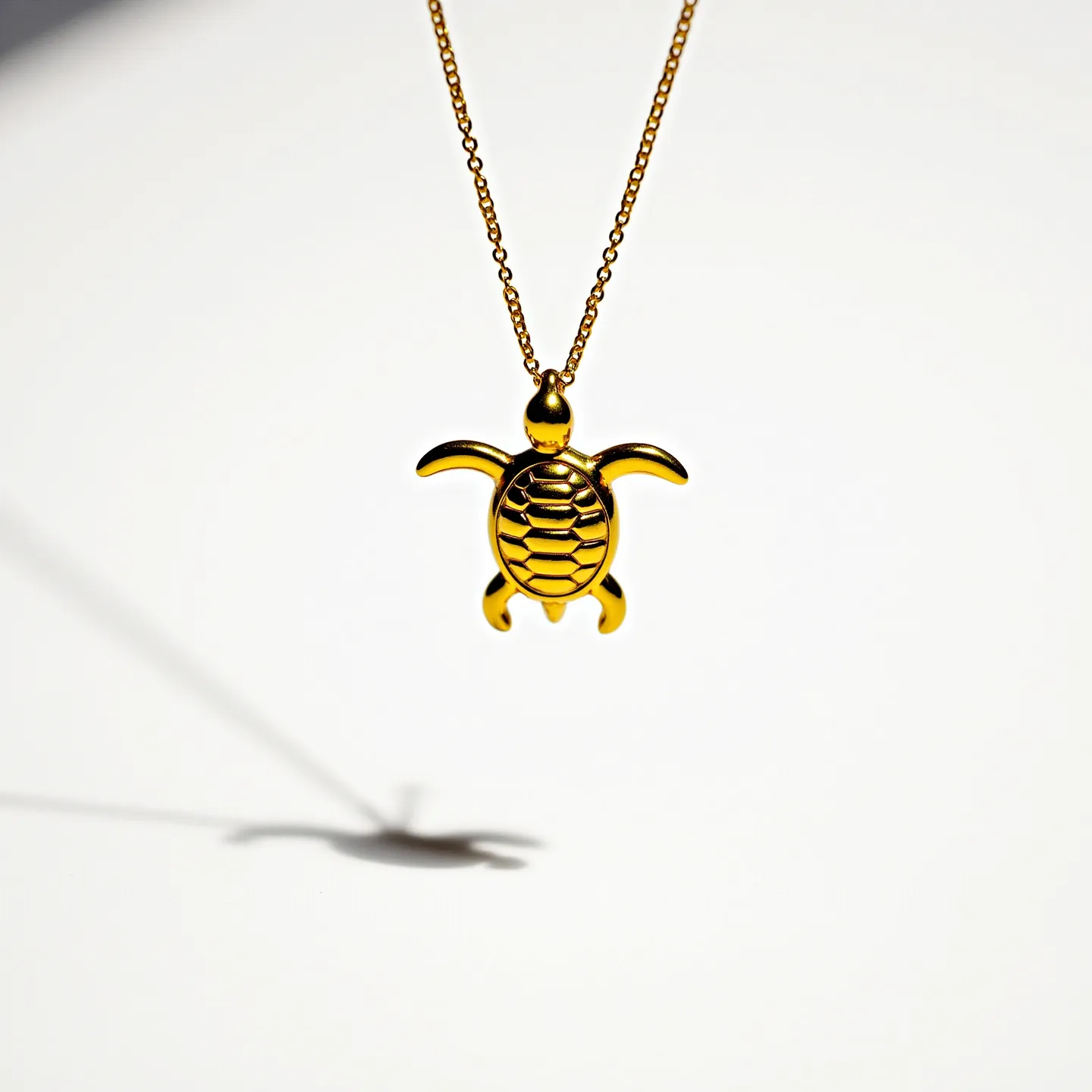 This turtle necklace features a pendant designed in the shape of a turtle, crafted from a polished metal with a gold finish that gives it a bright and reflective appearance. The necklace's chain is delicate and appears to be made from a matching gold-toned metal, with closely spaced links that complement the pendant's elegant simplicity. The turtle pendant is smooth and lacks any decorative stones or gems, highlighting the metalwork in its entirety. The attachment includes a simple loop at the top of the turtle where the chain threads through, ensuring the pendant remains securely in place when worn.