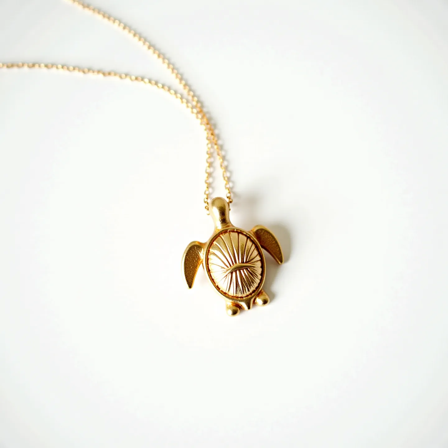 This turtle necklace features a pendant shaped like a turtle, crafted from a gold-toned metal that gives it a polished and elegant appearance. The turtle's shell is intricately detailed with a radial pattern carved into the metal, enhancing its texture and visual interest. The pendant is suspended from a delicate chain composed of fine links that match the pendant's golden hue, complementing the overall design. The necklace likely utilizes a conventional clasp mechanism, though this detail is not prominently visible. This accessory combines graceful design elements with a stylish representation of a turtle, making it suitable for both casual and formal wear.