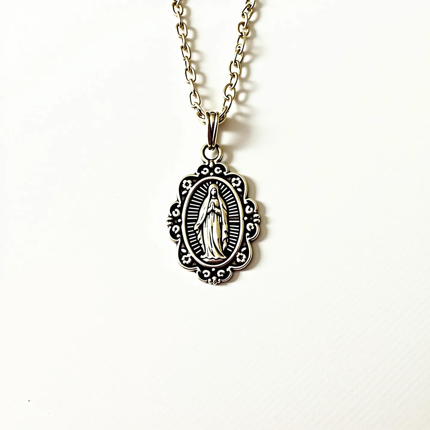 This Virgin Mary necklace features an intricately designed pendant, likely made of a silver-tone metal, depicting the figure of the Virgin Mary. The pendant has a scalloped edge with small bead-like details, adding an ornate touch. The necklace appears to have a sturdy, medium-sized chain with interconnected links, suggesting durability and comfortable wear. The pendant attachment is a simple loop, seamlessly integrated with the chain, allowing the pendant to hang gracefully. There are no visible gemstones or additional embellishments, giving the necklace a classic and elegant appearance. The clasp is not visible in the image, which might suggest a standard hook or clasp mechanism typical of necklaces of this design.