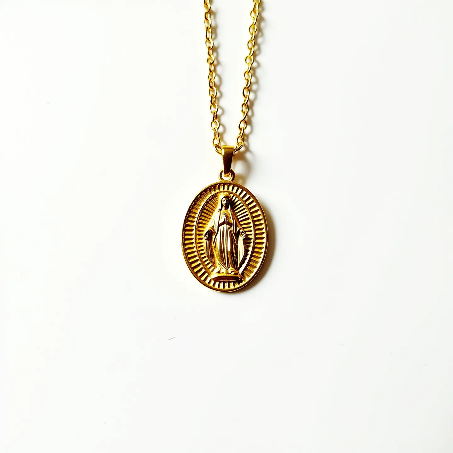 This Virgin Mary necklace features a gold-colored metal chain with a matching oval pendant. The pendant showcases an embossed image of the Virgin Mary, surrounded by a textured border that adds visual interest. The chain appears to be made of a simple, elegant link design, providing a classic and timeless look. The attachment mechanism likely consists of a standard lobster clasp, commonly used for its security and ease of use, though it is not visible in the image. There are no apparent gems or additional embellishments on the pendant, emphasizing its minimalist and devotional style.