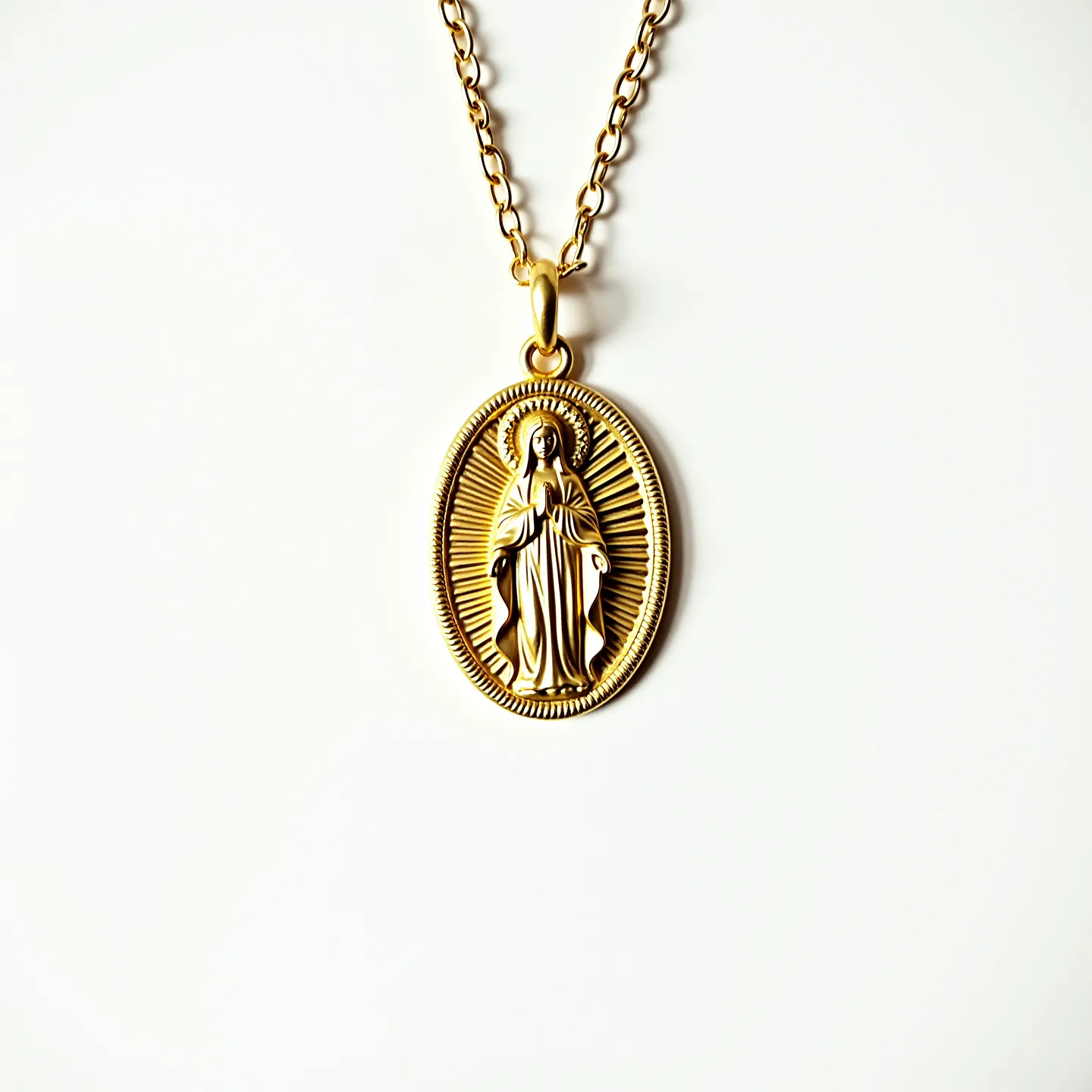 This virgin mary necklace features an elegantly crafted pendant made of gold-toned metal, showcasing a detailed depiction of the Virgin Mary. The pendant is oval-shaped, with intricate rays emanating from the figure, giving it a radiant appearance. The pendant is suspended from a chain composed of interlocking links that are also gold-toned, offering a cohesive and harmonious look. The attachment is a simple bail connector, allowing for easy movement along the chain. The overall design is both reverent and stylish, making it suitable for both casual and formal occasions.