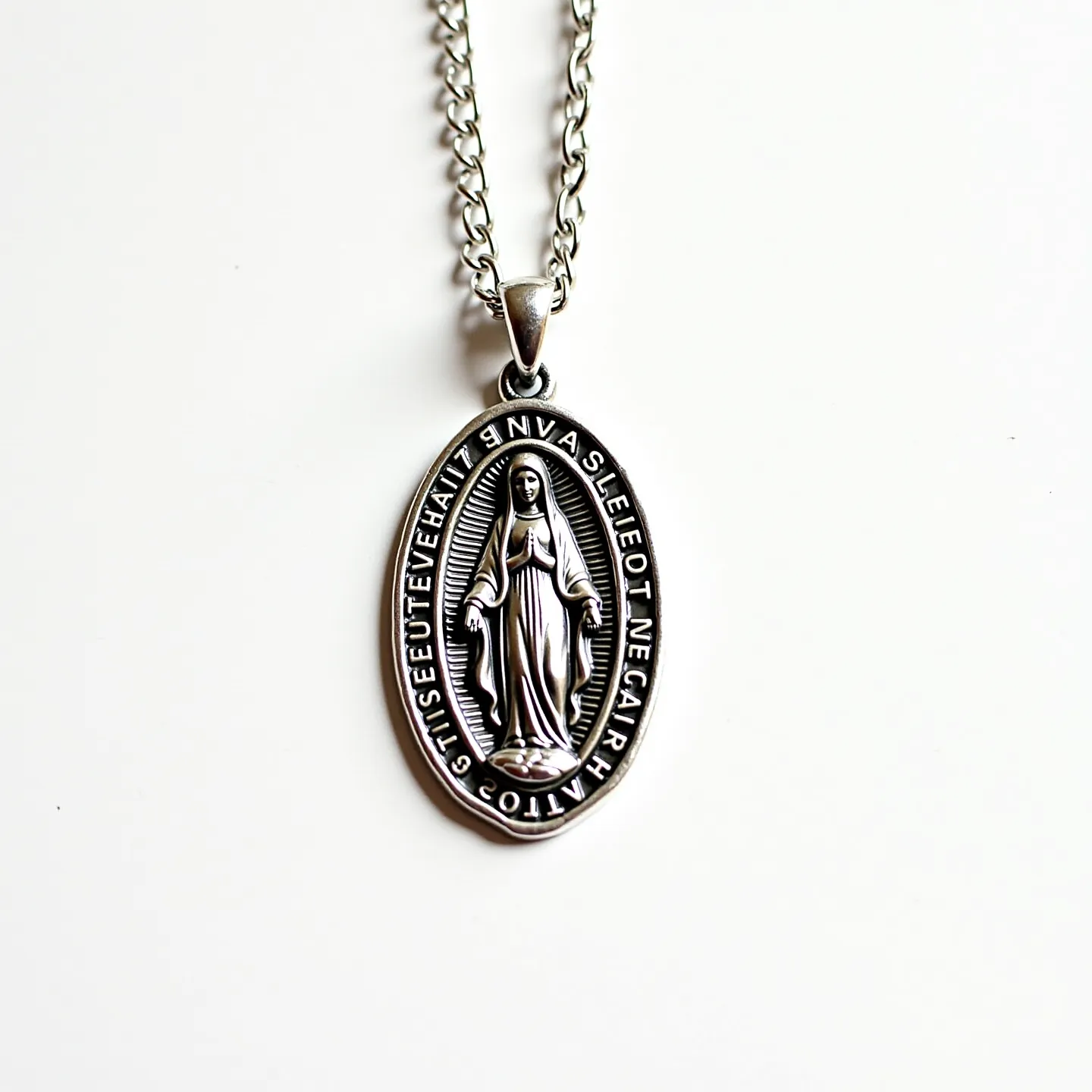 This Virgin Mary necklace features a silver-toned metal pendant depicting the Virgin Mary in relief, surrounded by an engraved inscription. The oval pendant is attached to a silver-toned chain via a small, polished bail. The chain is comprised of twisted links, giving it a textured appearance, and it closes with a standard lobster clasp for secure fastening. The pendant does not appear to feature any gemstones, instead relying on the detailed metalwork for its visual appeal. The overall design is classic and devotional, suitable for everyday wear or special occasions.