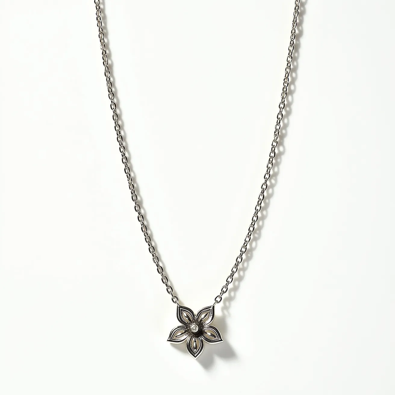 This white gold chain features a delicate link design, complementing the elegant pendant it supports. The pendant is crafted in the shape of a flower, with symmetrical petals that create a harmonious and balanced aesthetic. At the center of the flower is a small, round gem, likely a diamond, cut to enhance its brilliance and set securely within a bezel setting that emphasizes its central position. The chain is likely fastened with a standard clasp, ensuring ease of wear while maintaining the overall sophistication of the piece.