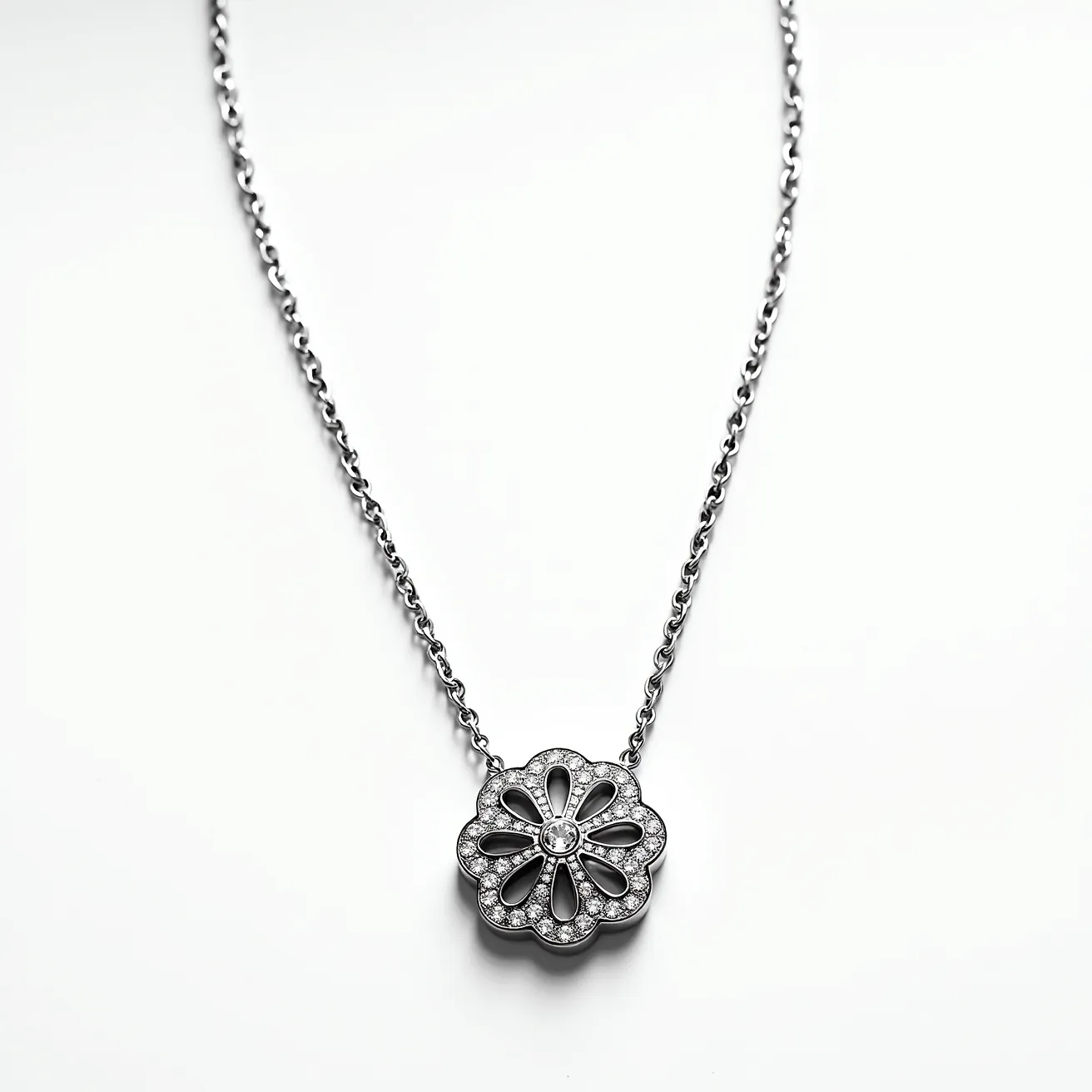 This white gold chain features a delicate, interlinked design that supports a central flower-shaped pendant. The pendant is intricately embellished with numerous small round-cut diamonds, which are set in a pavé style, enhancing the floral motif's elegance. At the center of the pendant, a larger round diamond is securely bezel-set, drawing the eye and adding a focal point of brilliance. The overall effect is sophisticated yet subtle, making it a versatile piece for various occasions. The chain is likely equipped with a secure clasp to ensure ease of use and durability, though the clasp type is not visible.