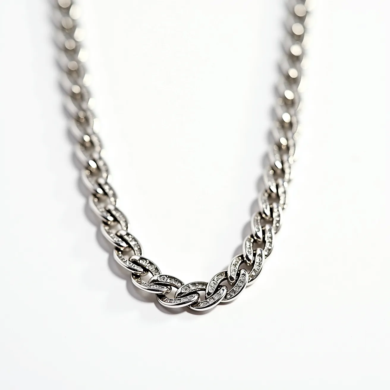 This white gold chain features a sophisticated, interlocking link design that exudes elegance and timeless style. The links are meticulously crafted to create a smooth, fluid appearance, reflecting the light from multiple angles. Each link is adorned with small, sparkling gems, likely diamonds, which are expertly set into the metal. The diamonds appear to be round cut and pave set, adding a subtle yet luxurious touch to the overall piece. The chain is finished with a secure clasp that ensures a comfortable fit while maintaining the chain's sleek and seamless look.