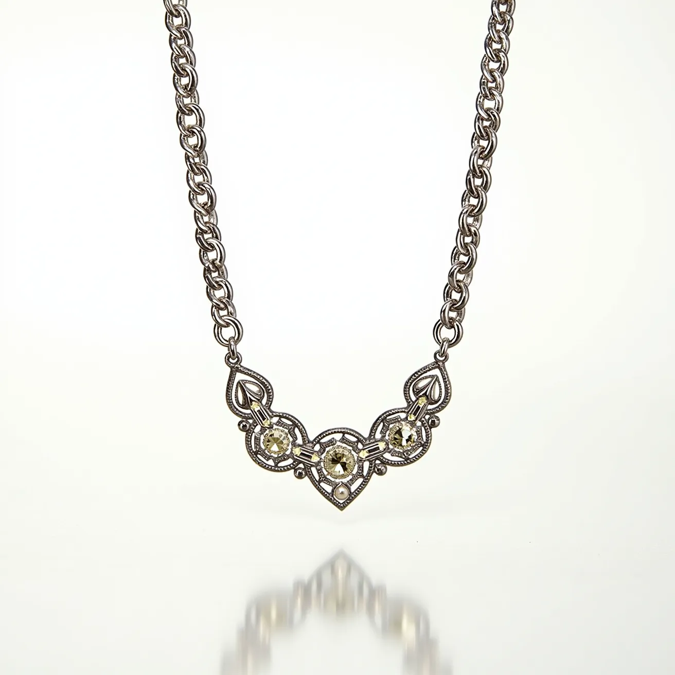 This white gold necklace features a captivating design with intricately crafted links leading to an ornate centerpiece. The central motif is adorned with sparkling gemstones, likely diamonds or clear stones, set in a precise arrangement to enhance their brilliance. Each gemstone is round-cut and securely set in a bezel or prong setting, surrounded by detailed metalwork that adds to the necklace's elegance. The chain is composed of interlocking links, ensuring durability and a smooth drape around the neck. A secure clasp, possibly a lobster or spring ring type, ensures the necklace remains fastened securely when worn.