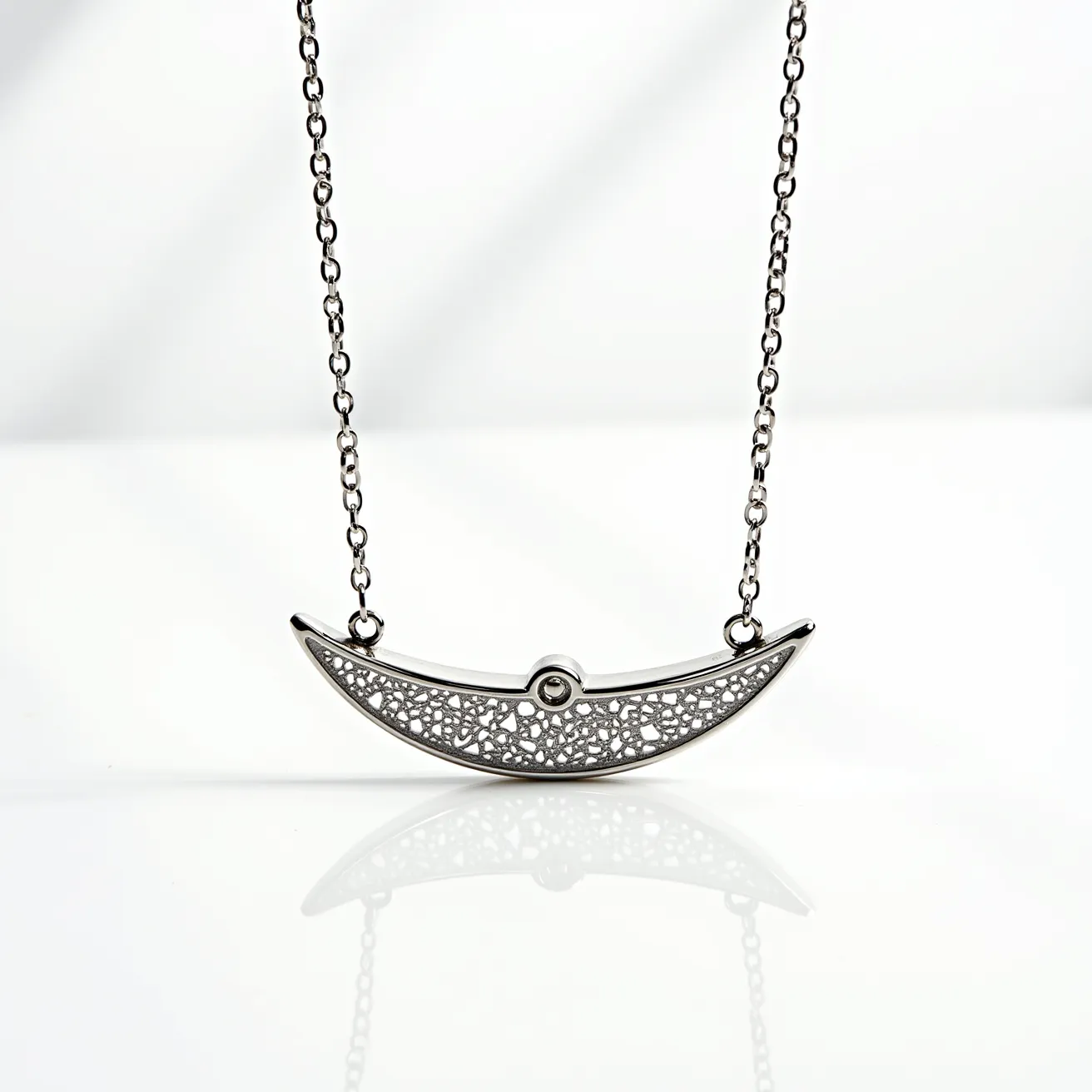 This white gold necklace features a delicate, intricately designed pendant that resembles a crescent moon. The pendant is adorned with a complex latticework pattern, providing an elegant and sophisticated look. At the center of the crescent, there is a small, round gemstone securely set, adding a subtle sparkle to the piece. The necklace is supported by a fine chain that complements the pendant, and it is likely equipped with a standard clasp for secure attachment. This exquisite necklace combines artistry with timeless materials, making it a notable piece of jewelry.