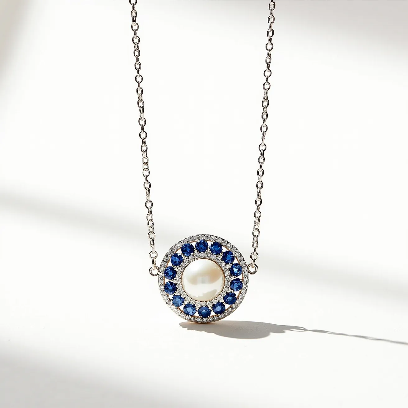 This white sapphire necklace features a central round pearl set within a circular pendant. The pearl is surrounded by a halo of small, round-cut blue sapphires, each carefully set in a prong setting. The pendant is suspended on a delicate silver chain, which complements the cool tones of the sapphires and the luster of the pearl. The necklace likely includes a discreet clasp mechanism integrated into the chain design, ensuring a secure and seamless attachment. The overall design showcases a harmonious balance of elegance and sophistication through its use of precious materials and classic gemstone arrangement.