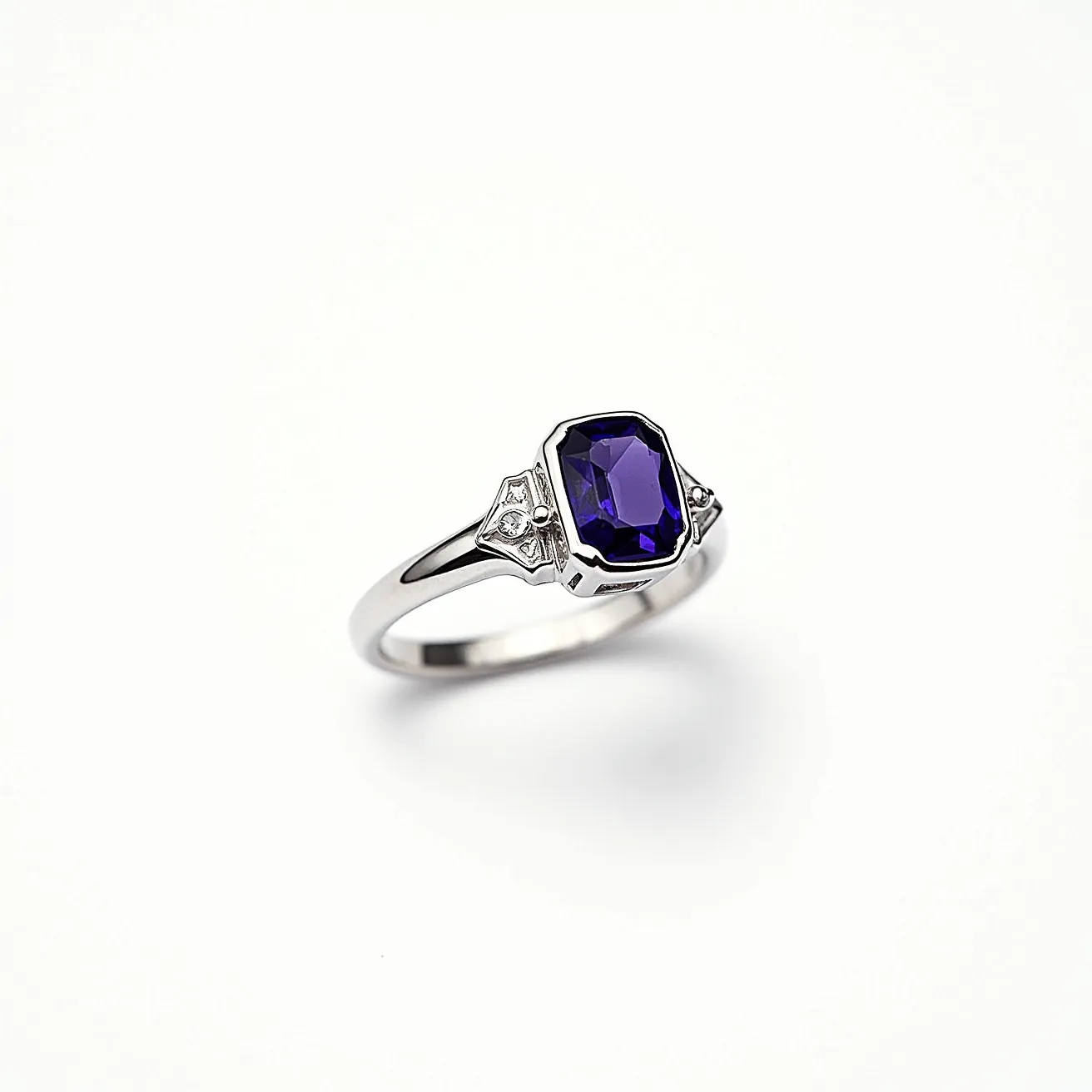 This alexandrite ring features a striking, faceted alexandrite gemstone, known for its color-changing properties, cut in an octagonal shape and securely set in a prong setting. The band appears to be made of a polished silver or white gold, complementing the gemstone with an elegant finish. The ring is adorned with intricate detailing on either side of the stone, incorporating small diamond-like accents that enhance the overall design. The setting provides a stable enclosure for the alexandrite, ensuring both security and style.