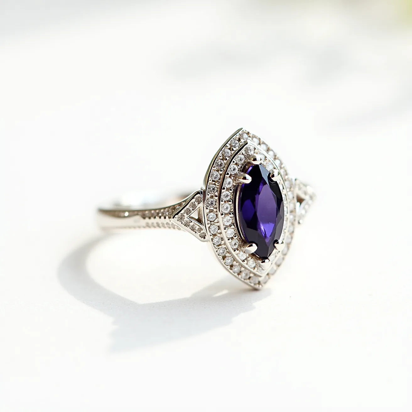 This alexandrite ring features a striking marquise-cut alexandrite as the centerpiece, secured by a four-prong setting. The gem is surrounded by a halo of small round diamonds, enhancing its brilliance and adding a touch of elegance. The band appears to be made of white gold or platinum, providing a sleek and sophisticated backdrop for the gemstones. The intricate detailing on the band and around the setting showcases craftsmanship, with additional diamond embellishments accentuating the overall design, adding to its luxurious appeal.