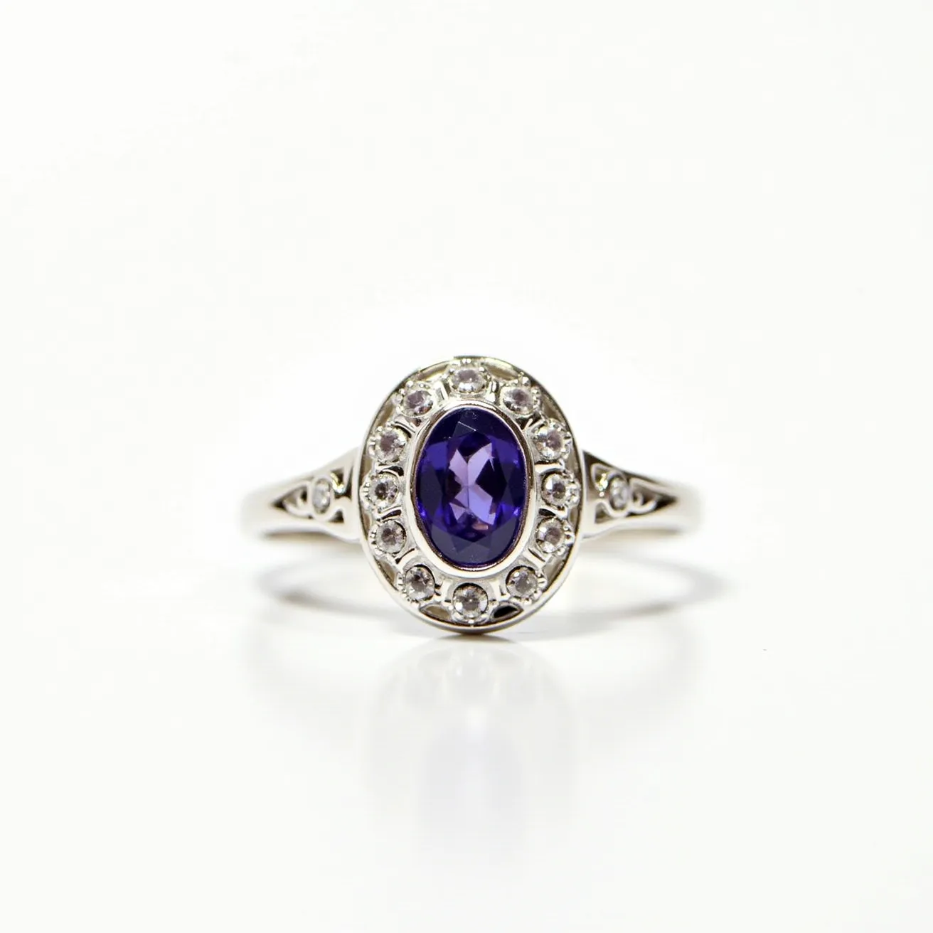 This alexandrite ring showcases an oval-cut alexandrite gem set at its center, exhibiting its characteristic color-changing properties. The gemstone is encircled by a halo of round brilliant-cut diamonds, enhancing its allure and brilliance. The setting appears to be crafted from white metal, likely platinum or white gold, providing a sleek and elegant backdrop that complements the gemstones. The band features delicate detailing, adding to the ring's overall sophistication and timeless elegance.