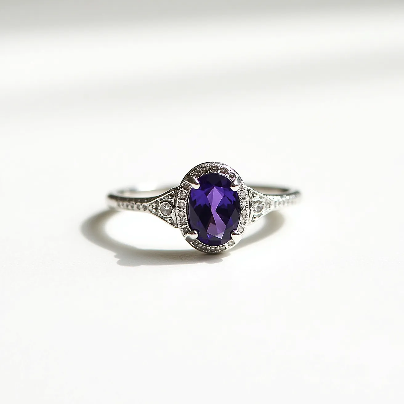 This alexandrite ring features a striking oval-cut gem set in an elegant platinum or white gold band. The gemstone, known for its color-changing properties, showcases a rich, deep hue. It is held securely by four prongs, expertly crafted to complement the stone's brilliance. Delicate detailing adorns the band, with small, round accent stones adding a touch of sparkle on either side of the central gem, further enhancing its allure and sophistication. The intricate design demonstrates a blend of classic and modern elegance, making it a standout piece of jewelry.