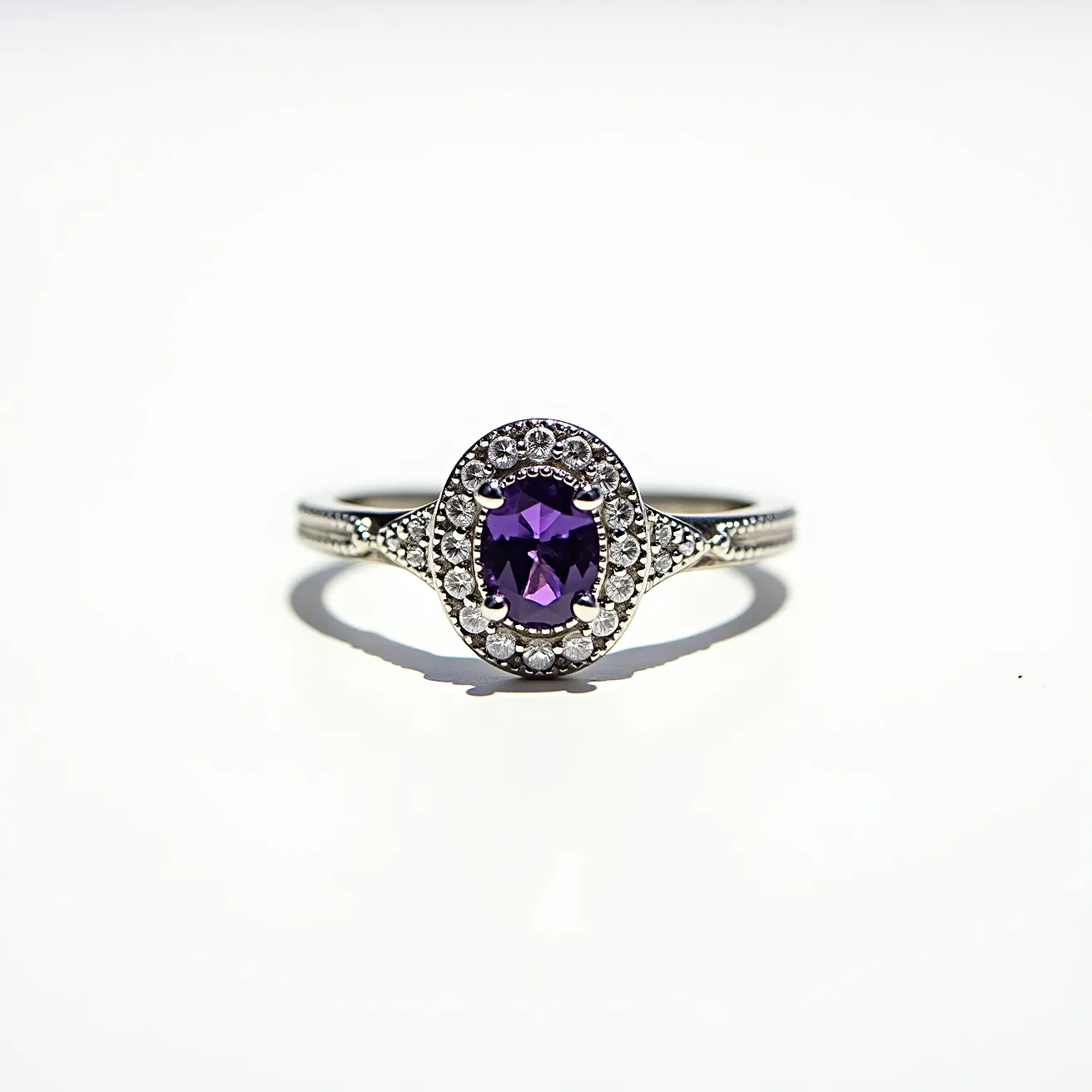 This alexandrite ring features an elegant design with a central oval-cut alexandrite gemstone set in a prong setting. Surrounding the main stone is a halo of small, clear round-cut diamonds, which are also set in prongs, enhancing the ring’s brilliance and sophistication. The band appears to be crafted from a white gold or platinum metal, adding a sleek and modern touch to the piece. The ring showcases intricate detailing on the shank, emphasizing its craftsmanship.