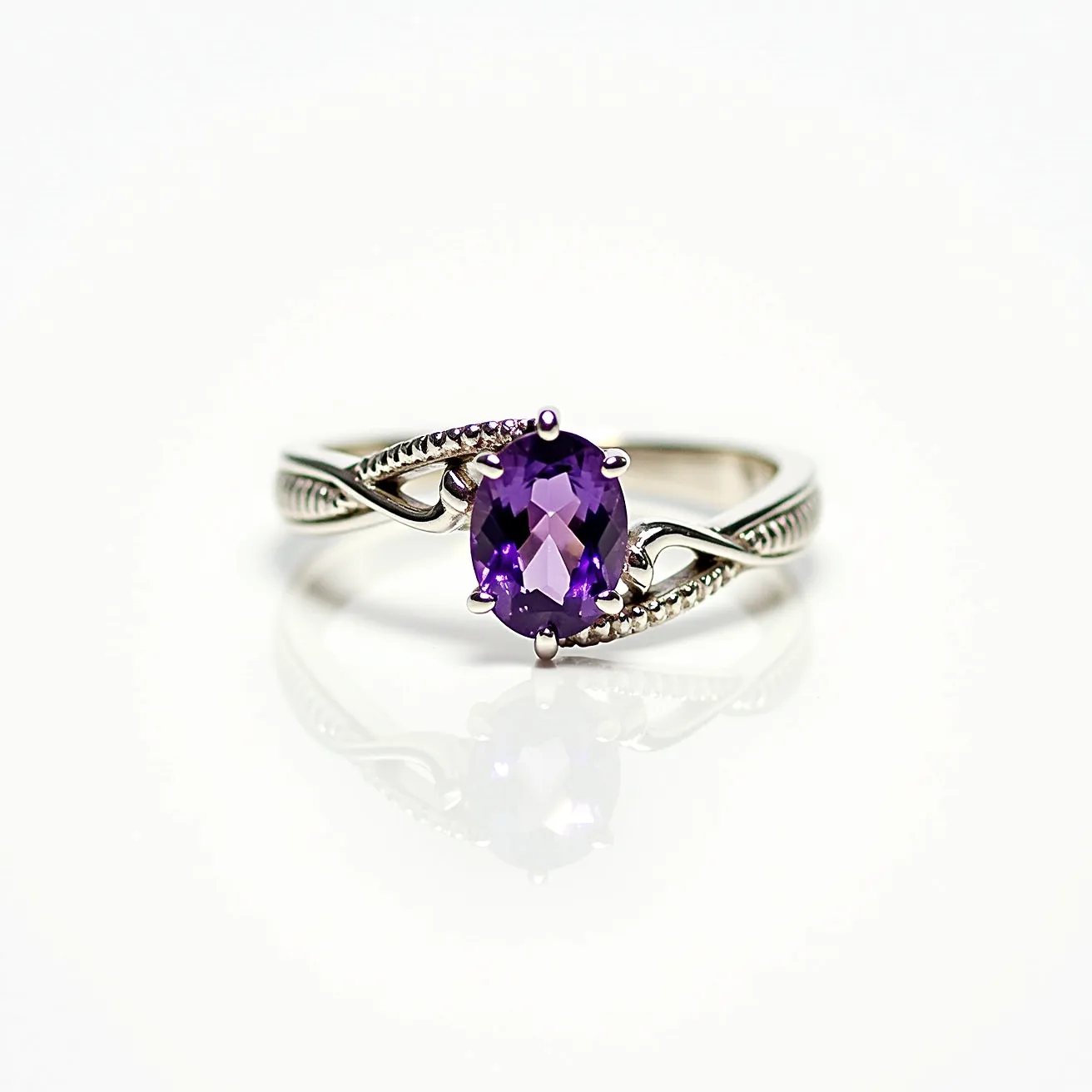 This amethyst promise ring features a prominent, oval-cut amethyst gemstone, showcasing a deep purple hue. The stone is securely set in a prong setting, highlighting its facets and enhancing its brilliance. The band of the ring is crafted from a lustrous metal, potentially silver or white gold, known for its elegant appearance. The design of the band includes delicate, intertwining details, adding a touch of sophistication and charm to the overall aesthetic. This intricate detailing on the band complements the centerpiece amethyst, making it an eye-catching piece of jewelry.