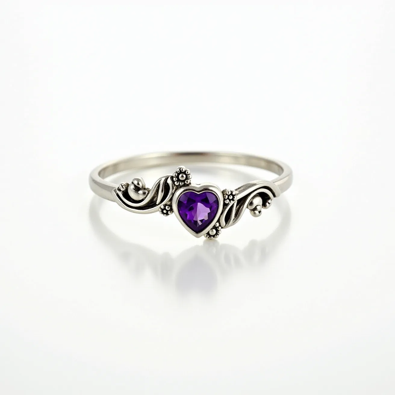 This amethyst promise ring features a delicate heart-shaped amethyst as its centerpiece, set in a stylish bezel setting. The band is crafted from a silvery metal, possibly sterling silver, which complements the deep purple hue of the gemstone. Ornate detailing surrounds the amethyst, adding an elegant touch with swirling designs and small, bead-like accents. The intricate craftsmanship of the band enhances the ring's elegant aesthetic, making it a charming symbol of commitment.