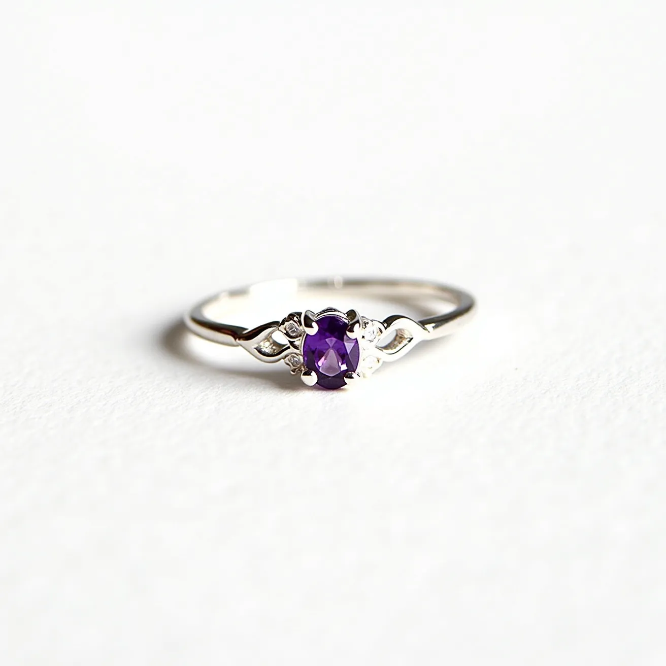 This amethyst promise ring features a beautifully cut oval amethyst set in a prong setting that accentuates its rich purple hue. The band, likely crafted from a polished metal such as sterling silver or white gold, is designed with delicate details on either side of the gemstone, adding an elegant touch to its overall appearance. The design incorporates subtle yet intricate elements that enhance the central amethyst, making it stand out as a symbol of commitment and promise.