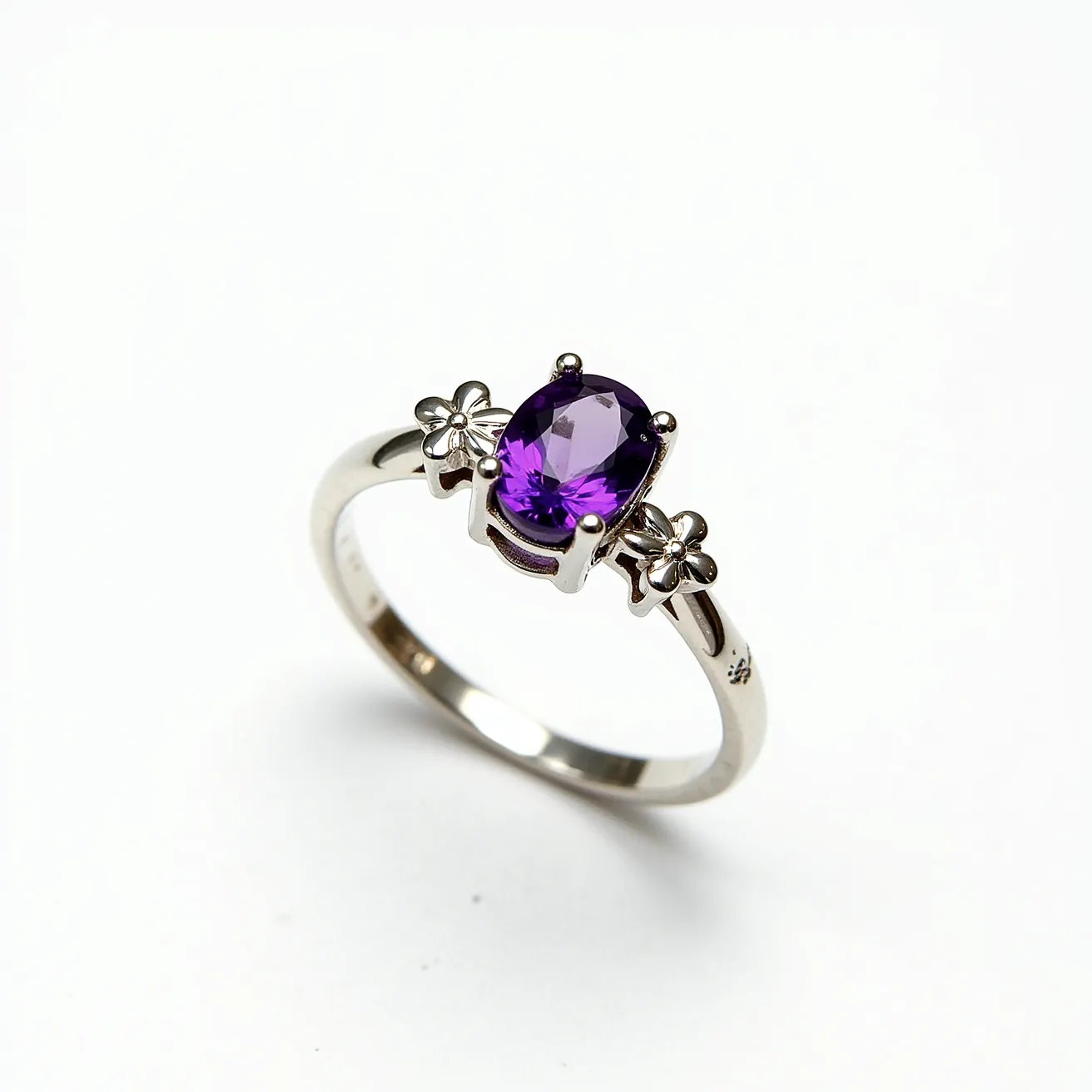 This amethyst promise ring features a beautifully cut oval amethyst gemstone, securely set in a four-prong setting. The vibrant purple of the amethyst is complemented by a band made from a polished metal, possibly sterling silver, giving the ring a sleek and elegant appearance. On either side of the central gemstone are small floral accents, adding an element of charm and sophistication to the overall design. The band's material and design suggest durability and style, making it suitable for everyday wear.