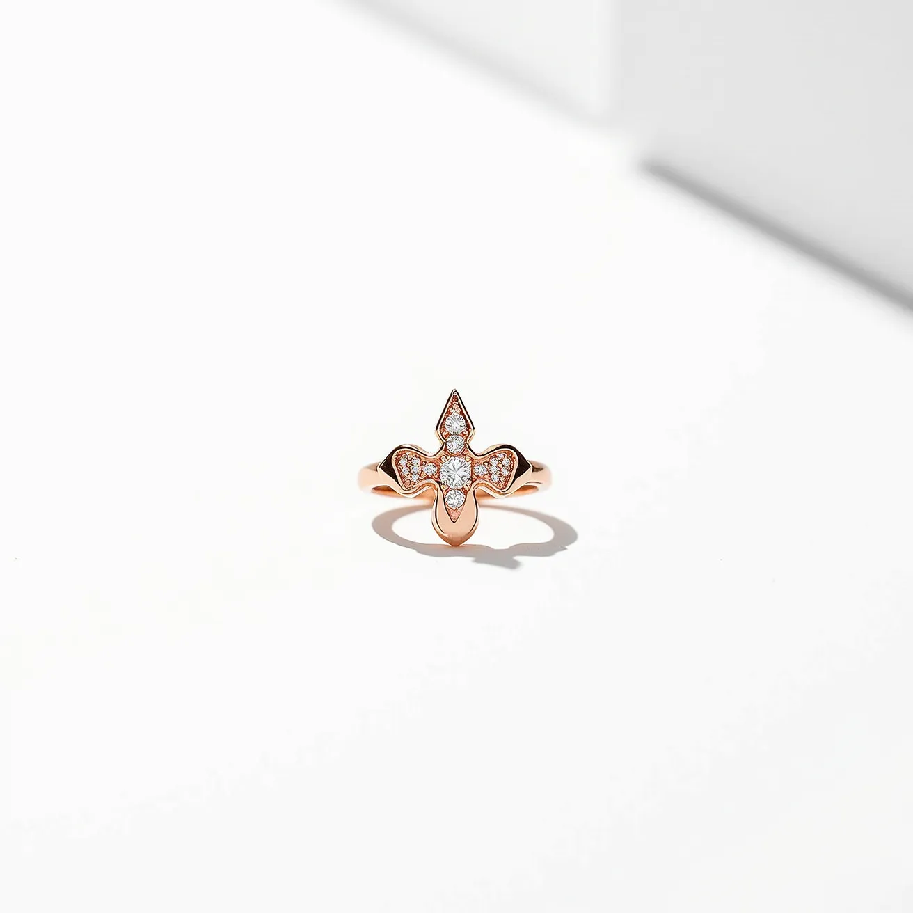 This angel ring is crafted from a lustrous rose gold metal, featuring an intricate cross-like design as its centerpiece. The centerpiece is embellished with small, clear round-cut gemstones, likely diamonds or cubic zirconia, set in a pavé style that enhances their sparkle and elegance. The band of the ring is smooth and polished, adding to its refined appearance. The ring's design does not incorporate any clasps or attachments, emphasizing its classic and seamless look.